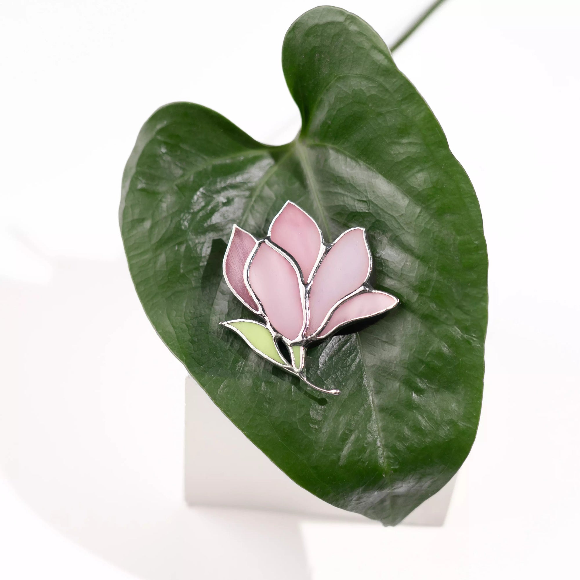 Magnolia stained glass brooch on a green leaf
