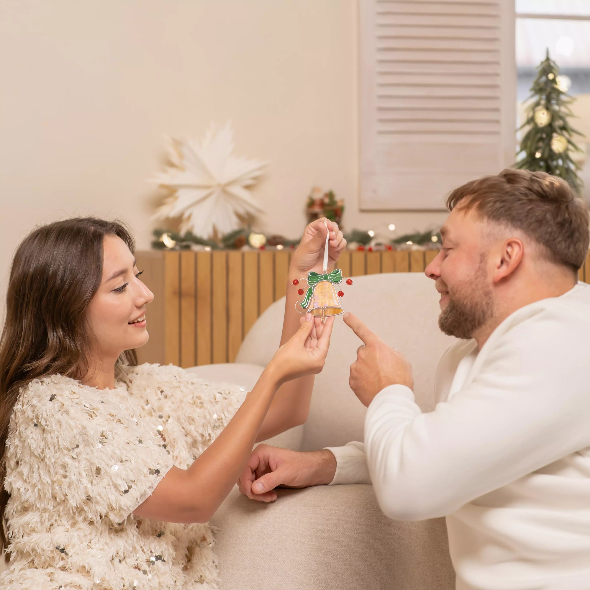 Man and woman holding stained glass bell together in a cozy living room.