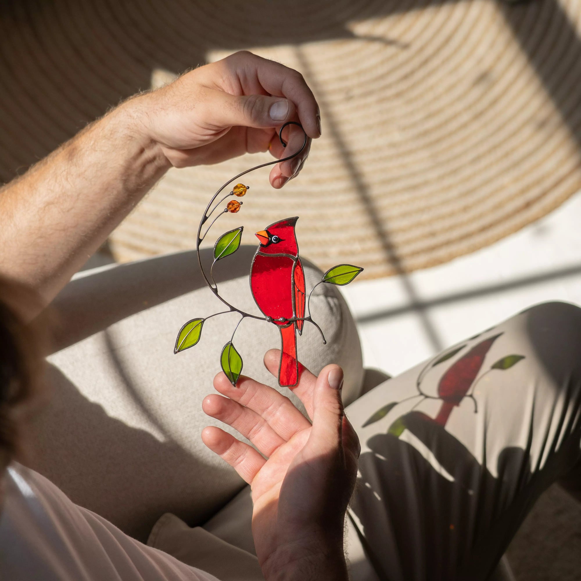 Hand holding a stained glass red cardinal bird on a branch with leaves.