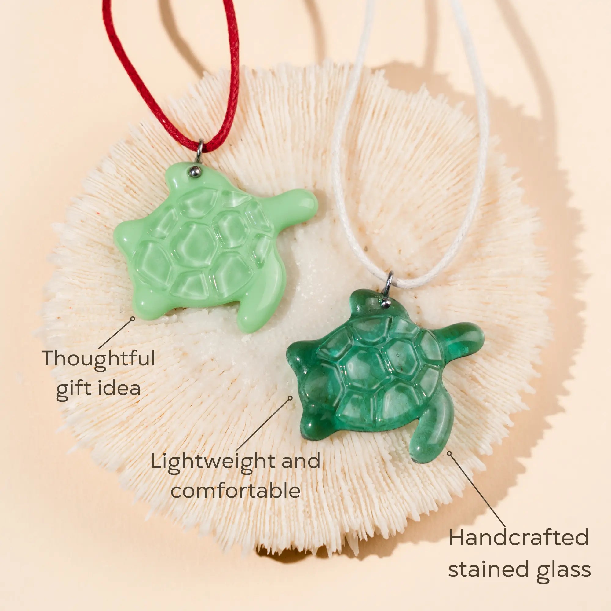 Two green turtle stained glass necklaces on a shell as a thoughtful gift idea