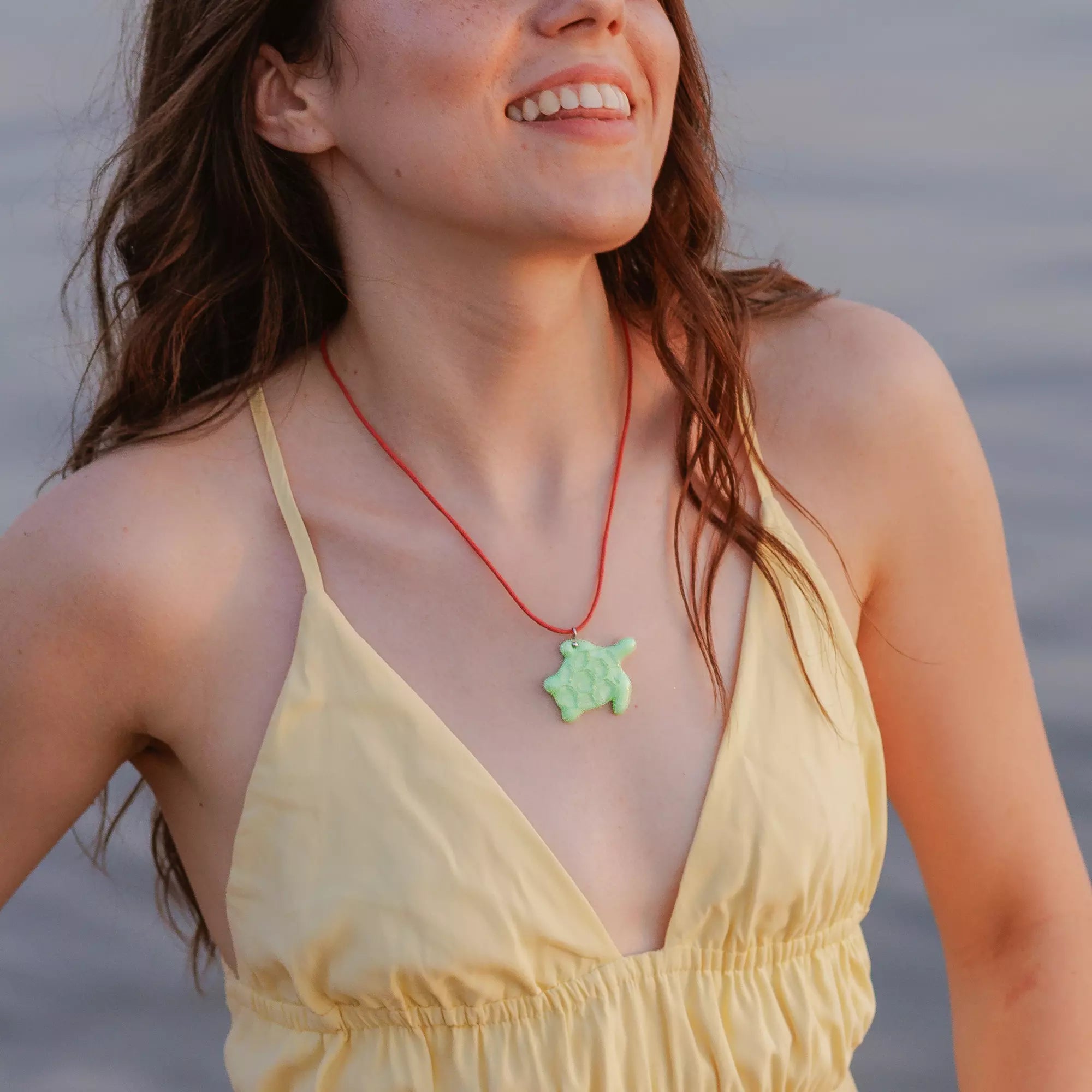 Woman wearing a yellow dress and red necklace with mint stained glass pendant by a body of water.