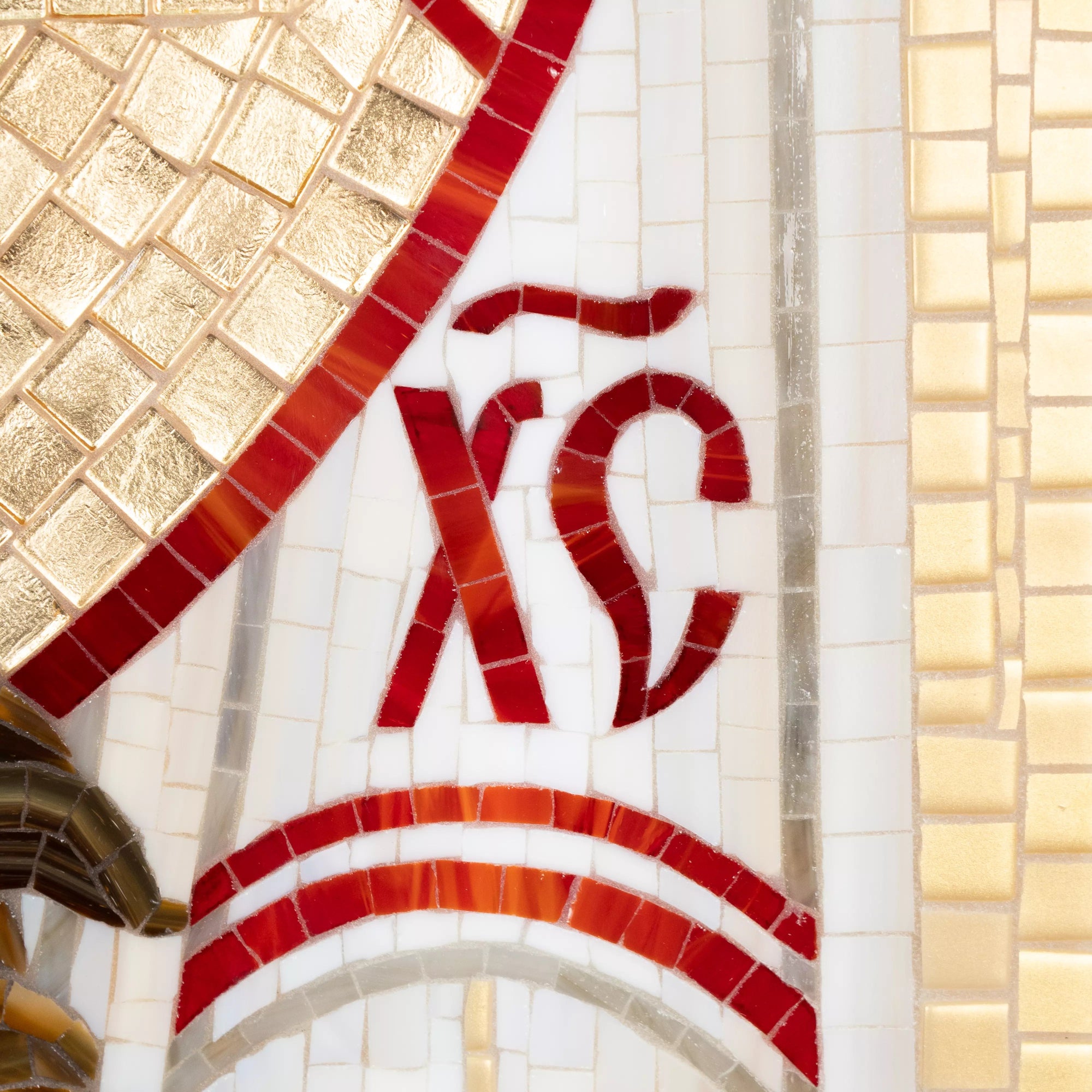 Stained glass mosaic design with red and gold XC letters on a wall