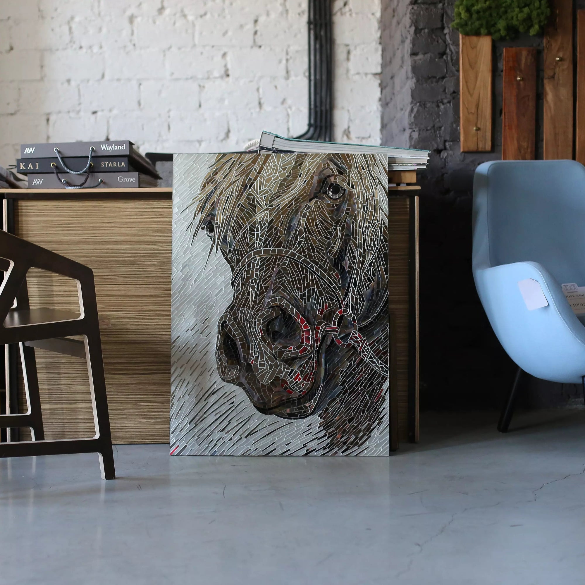 Horse mosaic resting against a desk in a modern office with blue chair and books