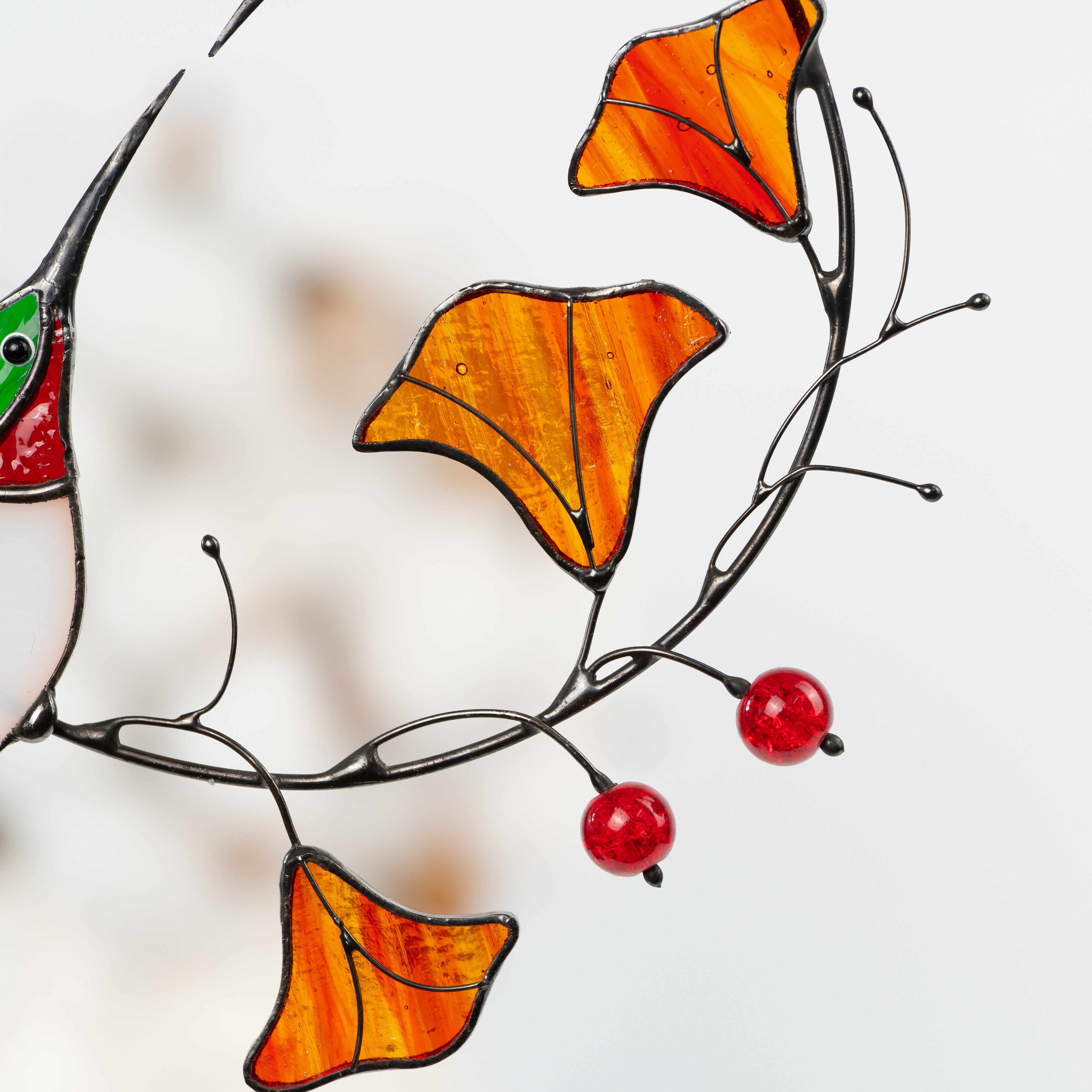 Close-up of orange stained glass flowers and red glass berries on black metal vine