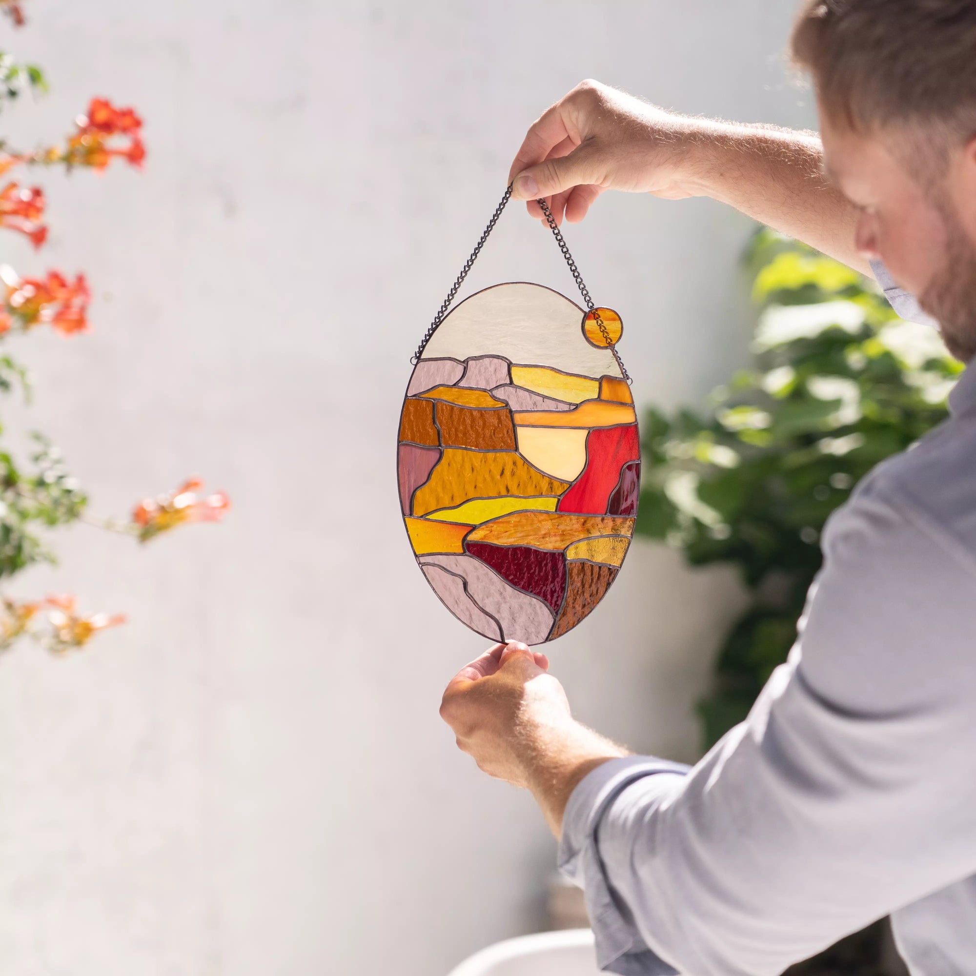 Man lifting oval stained glass sunset panel with yellow, red and earthy stained glass details