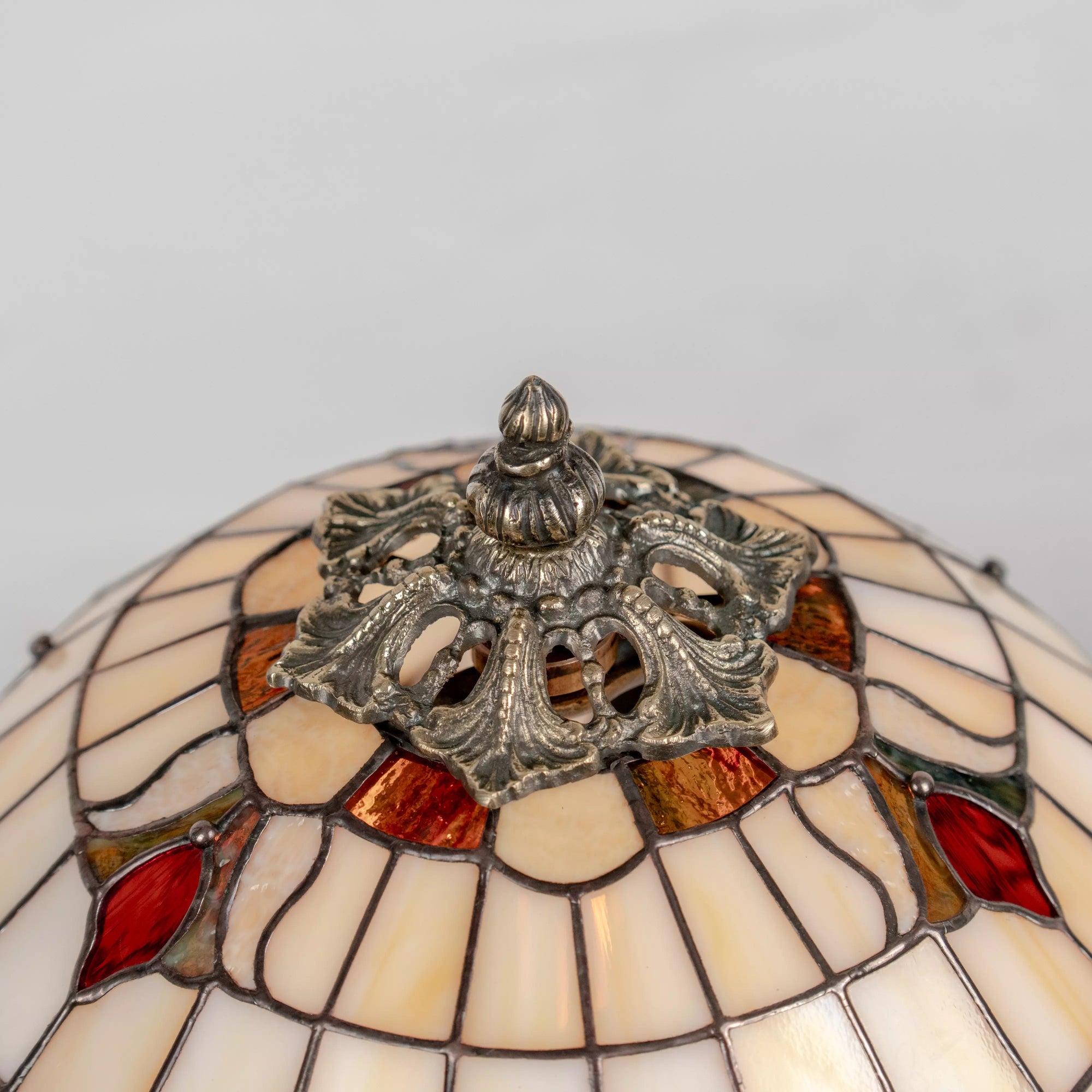 Lamp finial and cap with bronze finish, surrounded by cream and amber stained glass pieces