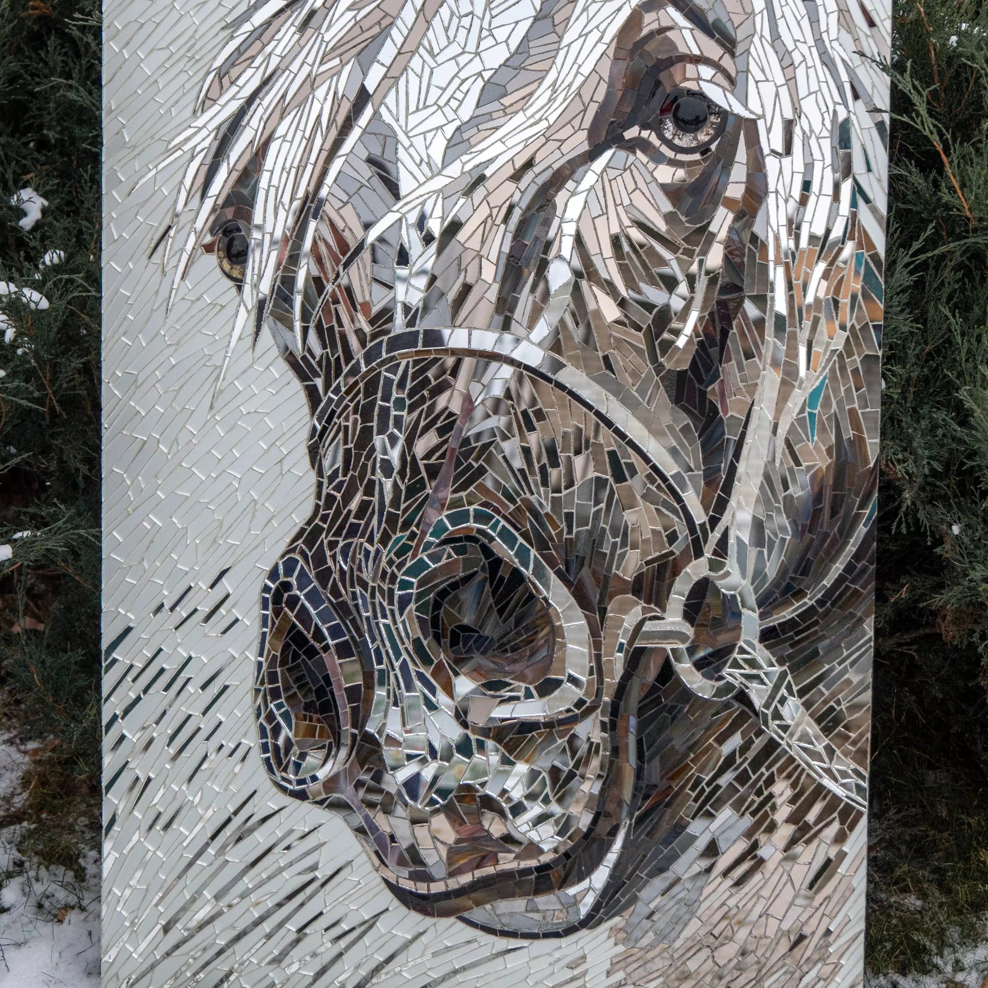 Horse head mosaic panel placed outdoors in snow against green bushes