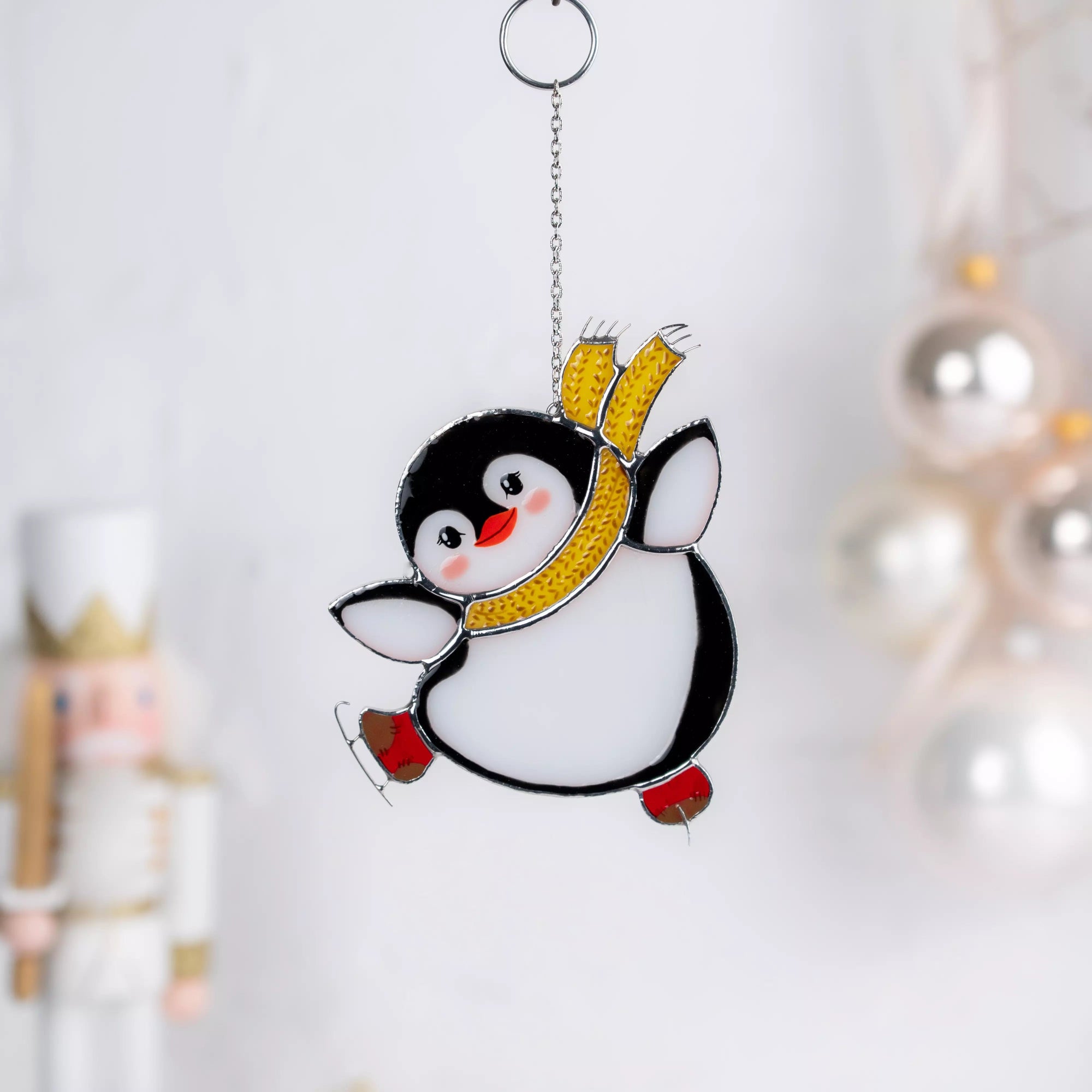 Penguin stained glass suncather with a yellow scarf and red skates on a white background