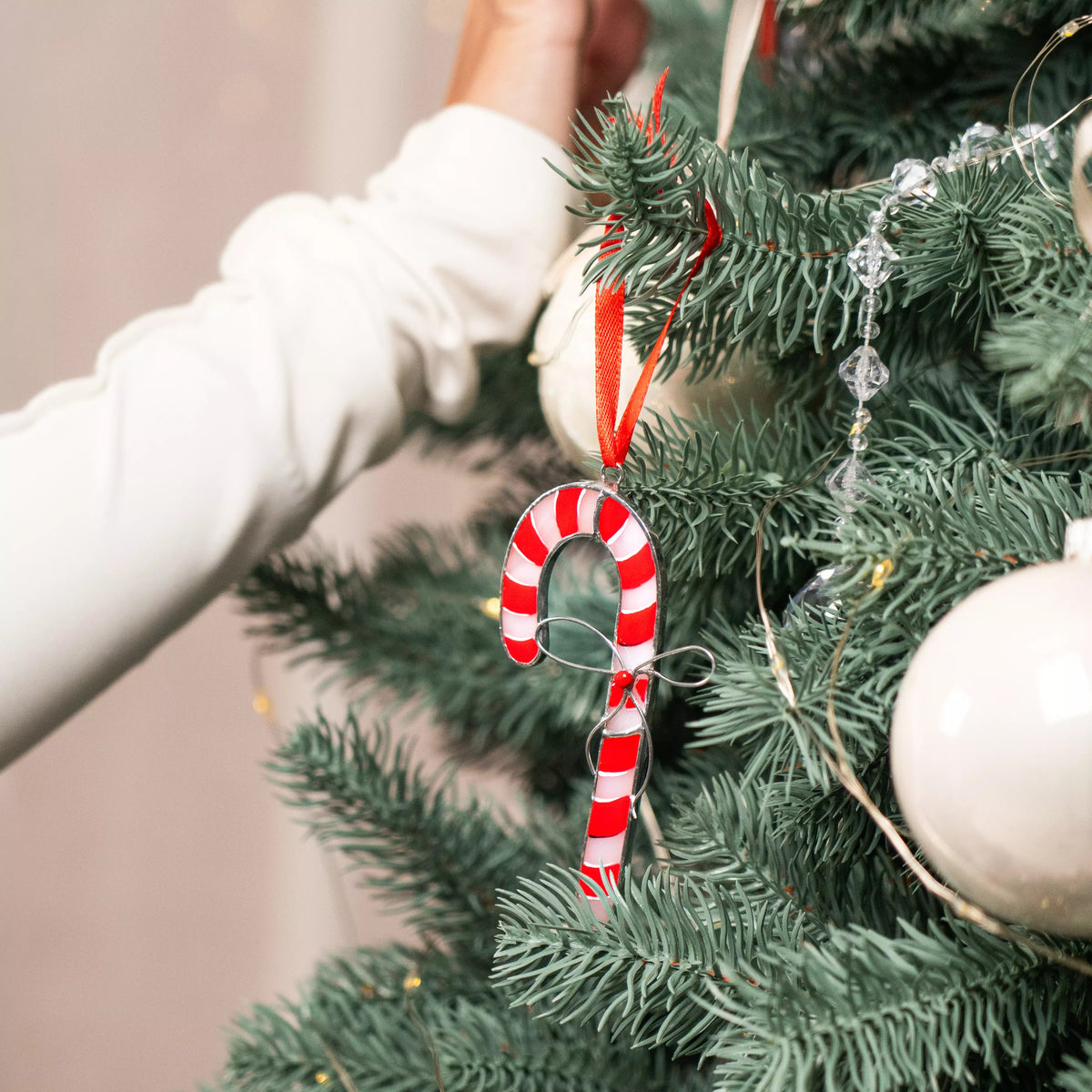 Hands decorating a Christmas tree with a candy cane stained glass ornament.