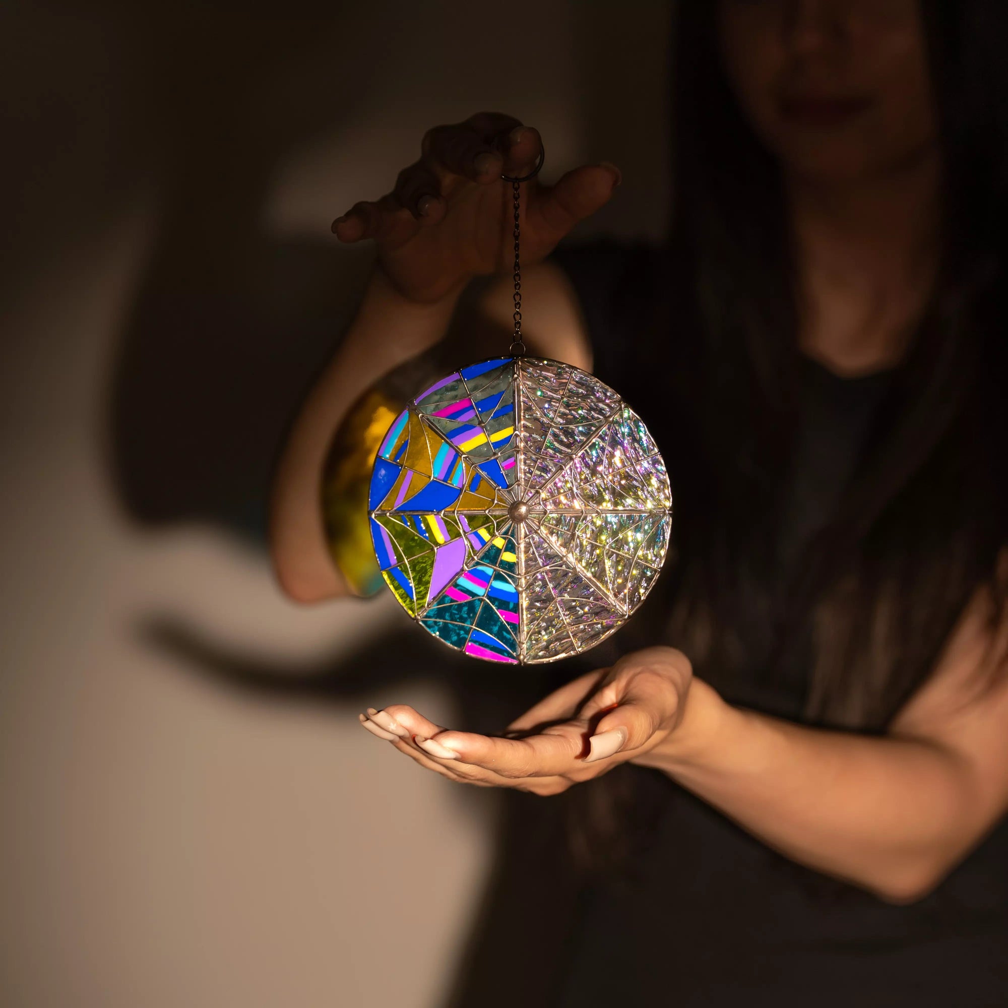 Bright stained glass round suncatcher glowing in hand against shadowed wall
