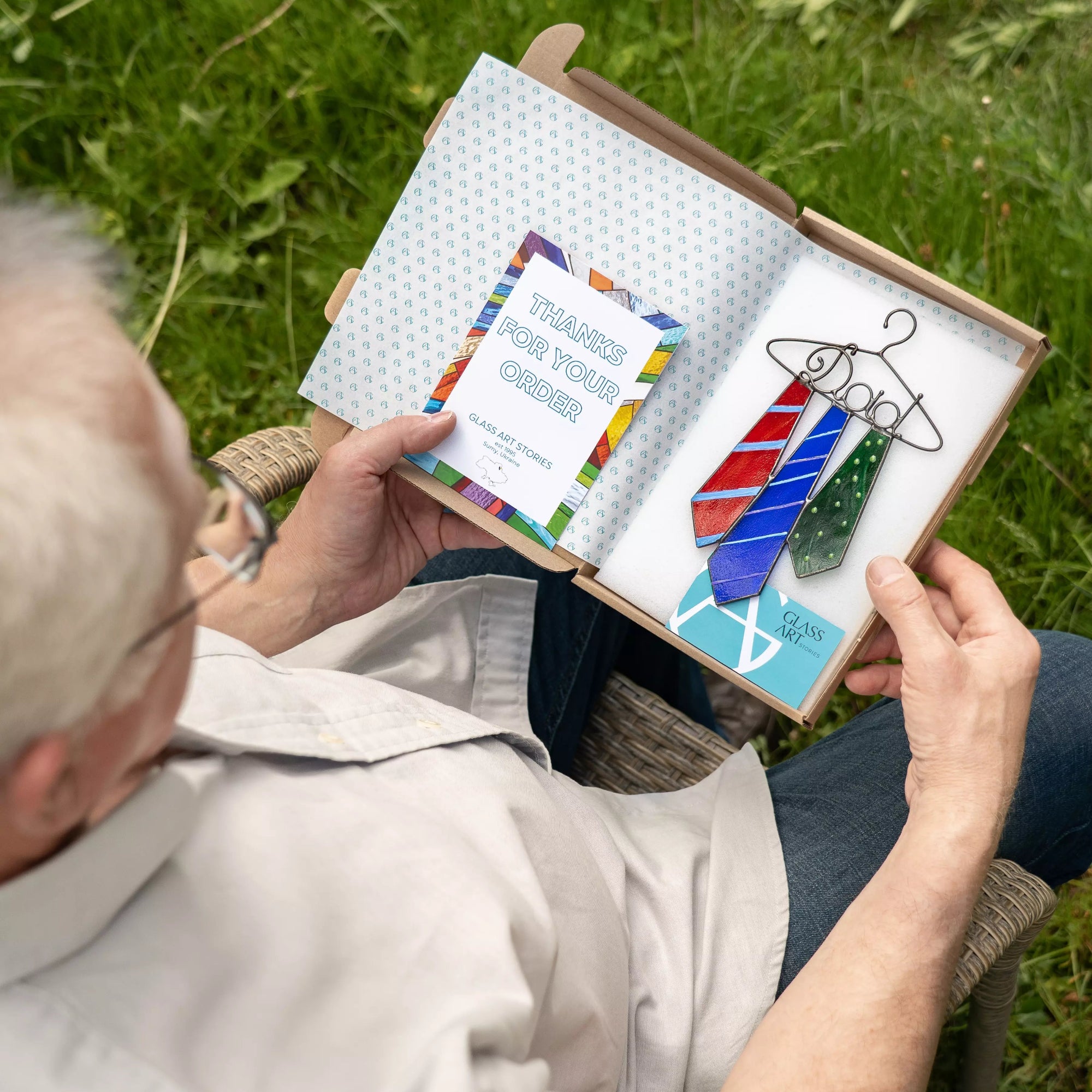 Person holding a box with tie suncatcher and a thank you card outdoors.