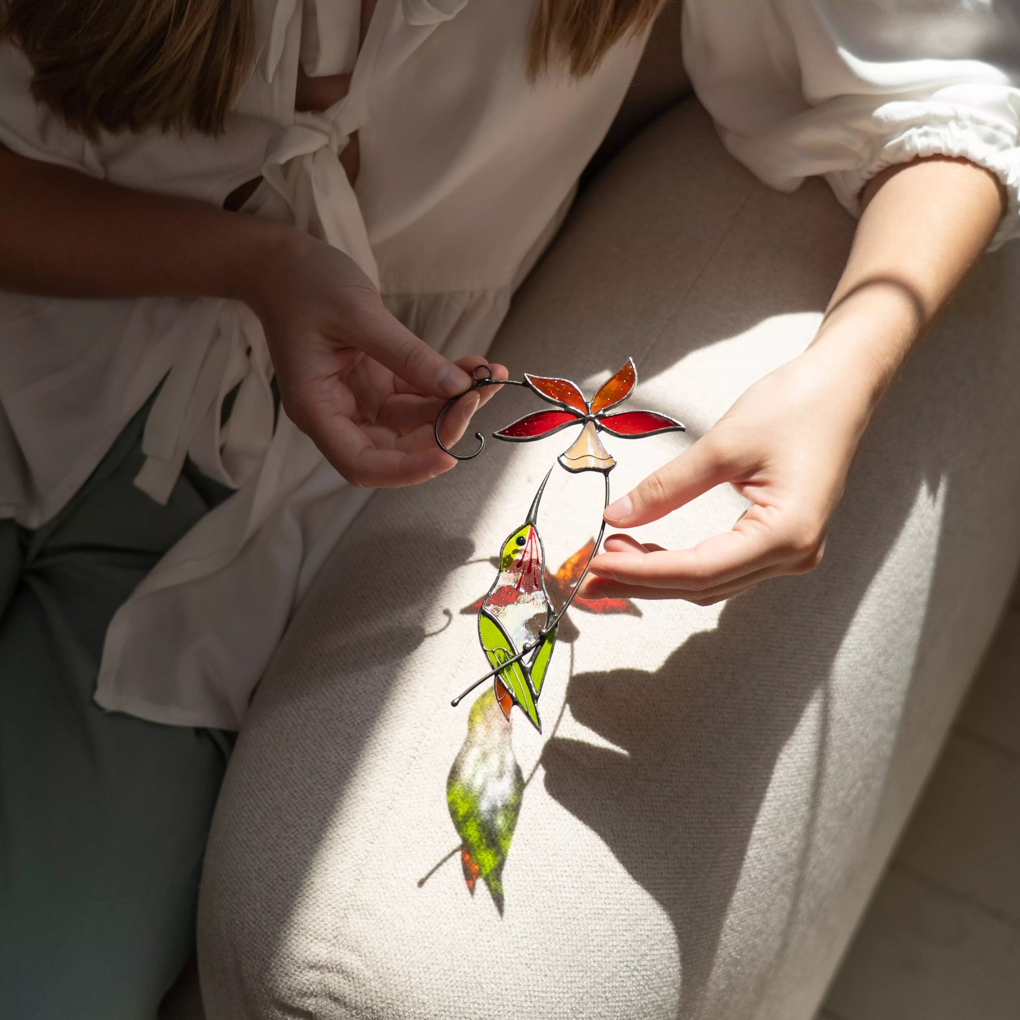 Person holding a bright stained glass hummingbird and bell flower decoration.