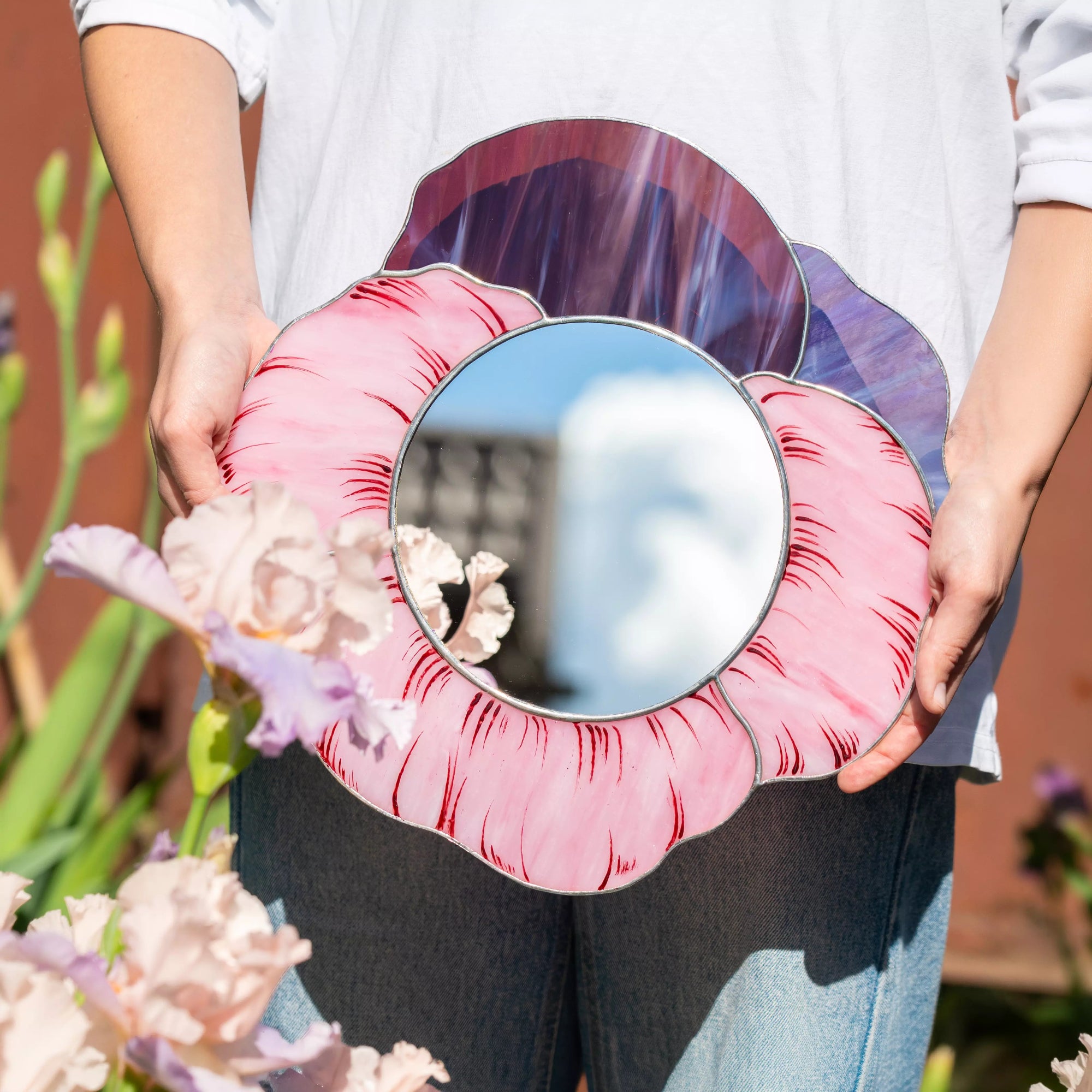 Person holding stained glass mirror with a pink floral design outdoors.