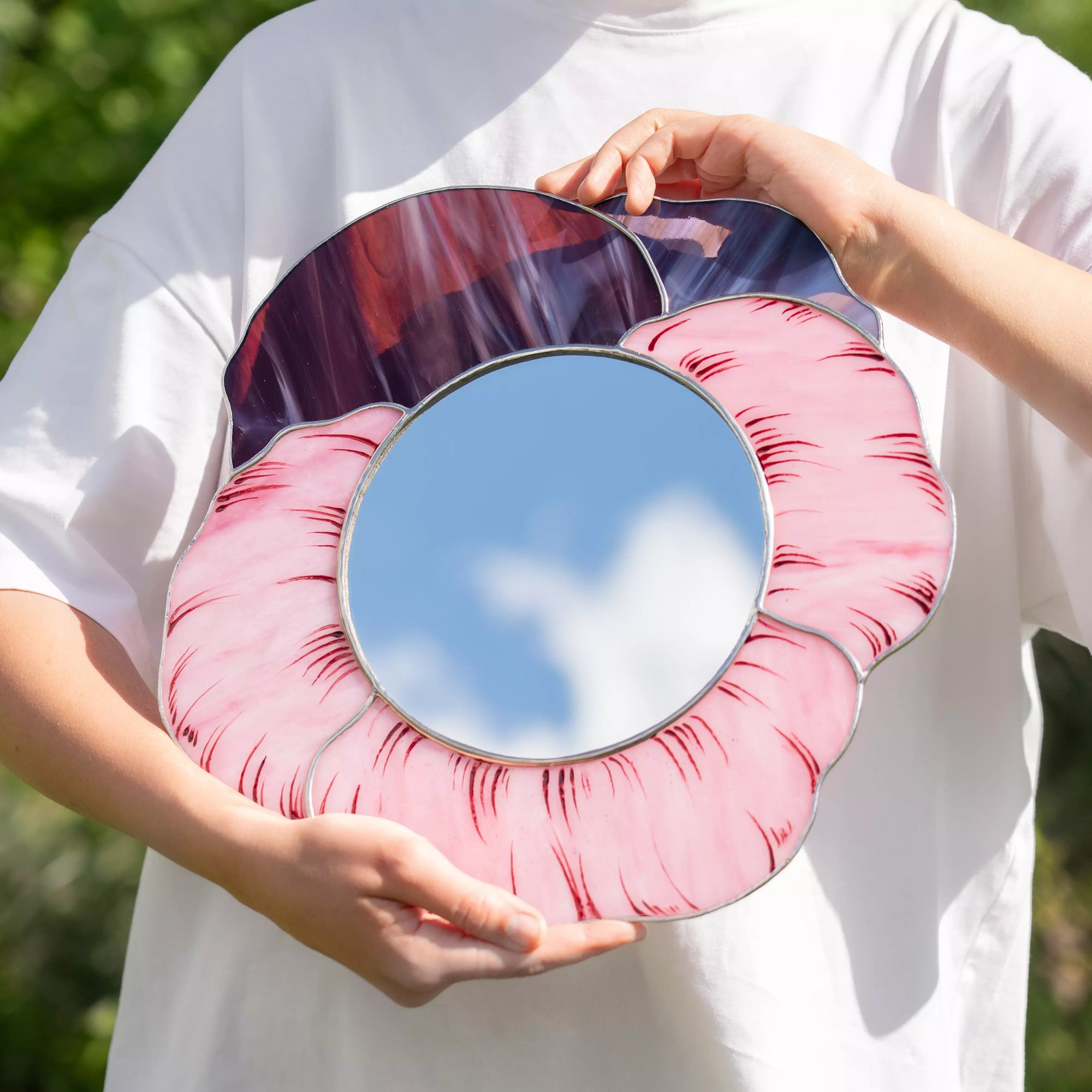 Person holding stained glass mirror with a pink floral design outdoors