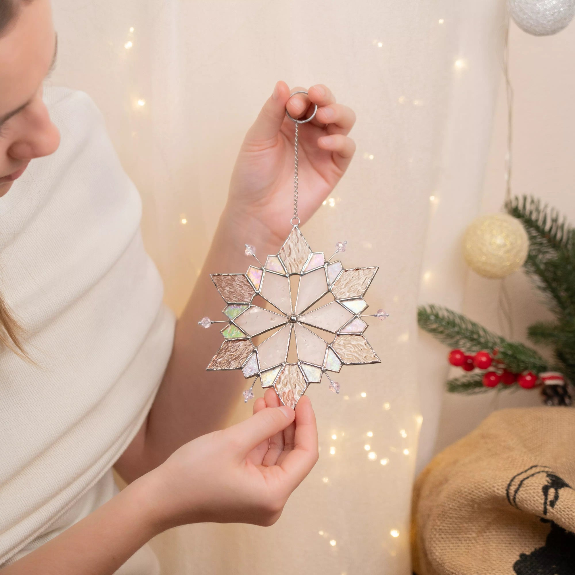 Person holding stained glass snowflake with pink beads ornament on a festive background
