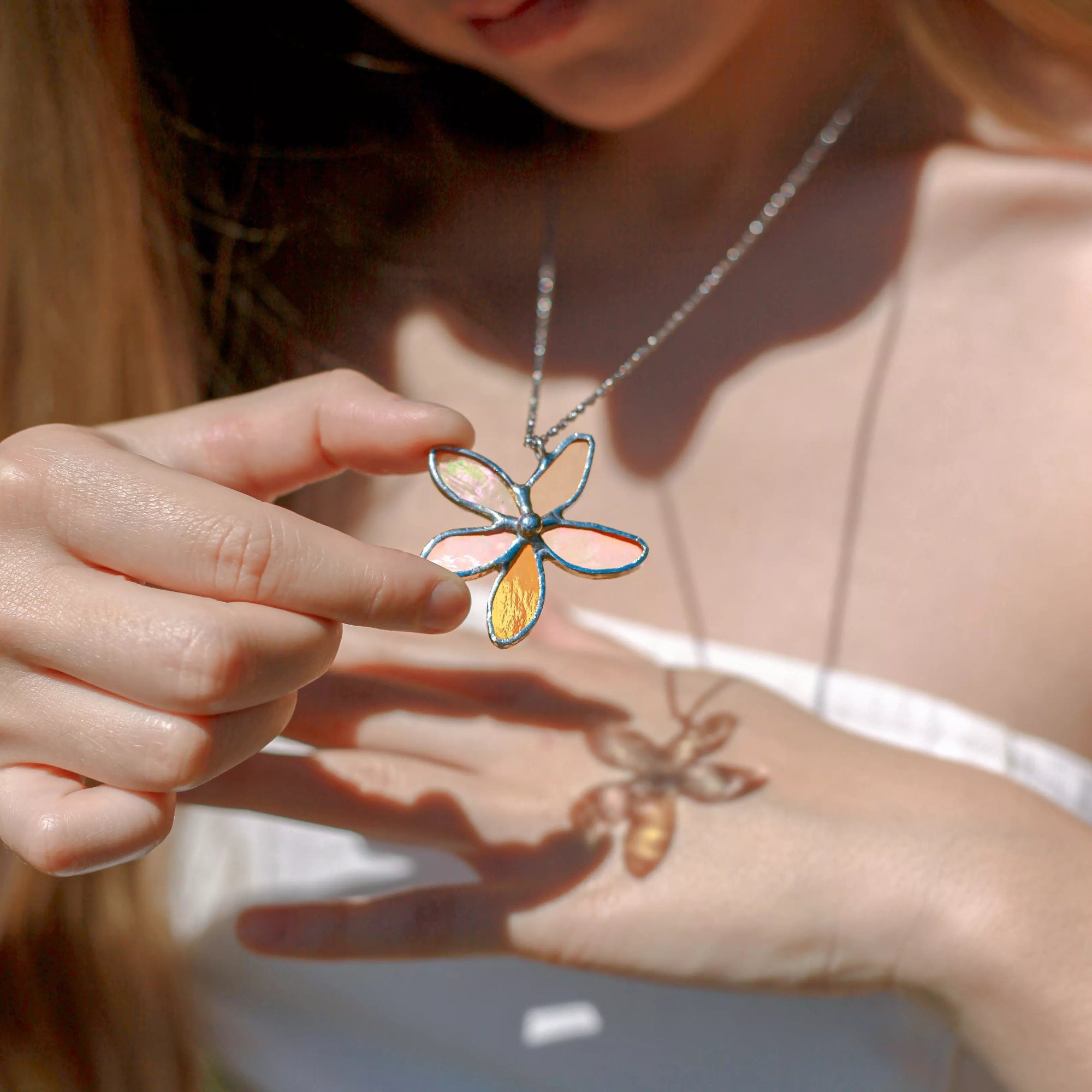 Person holding a flower-shaped stained glass pendant, that casts a colorful shadow on the other hand