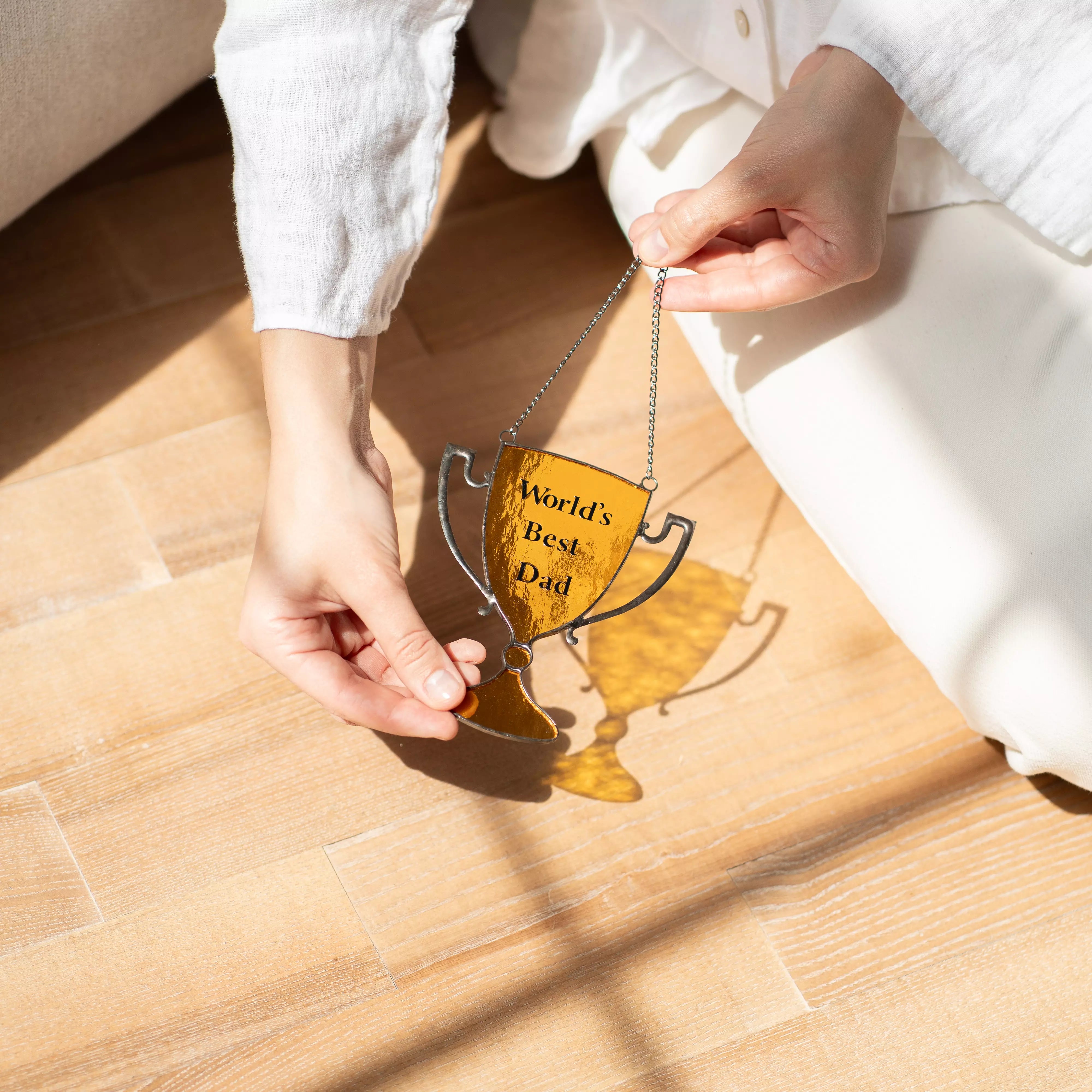 Person holding a stained glass ornament with 'World's Best Dad' text on a wooden floor.