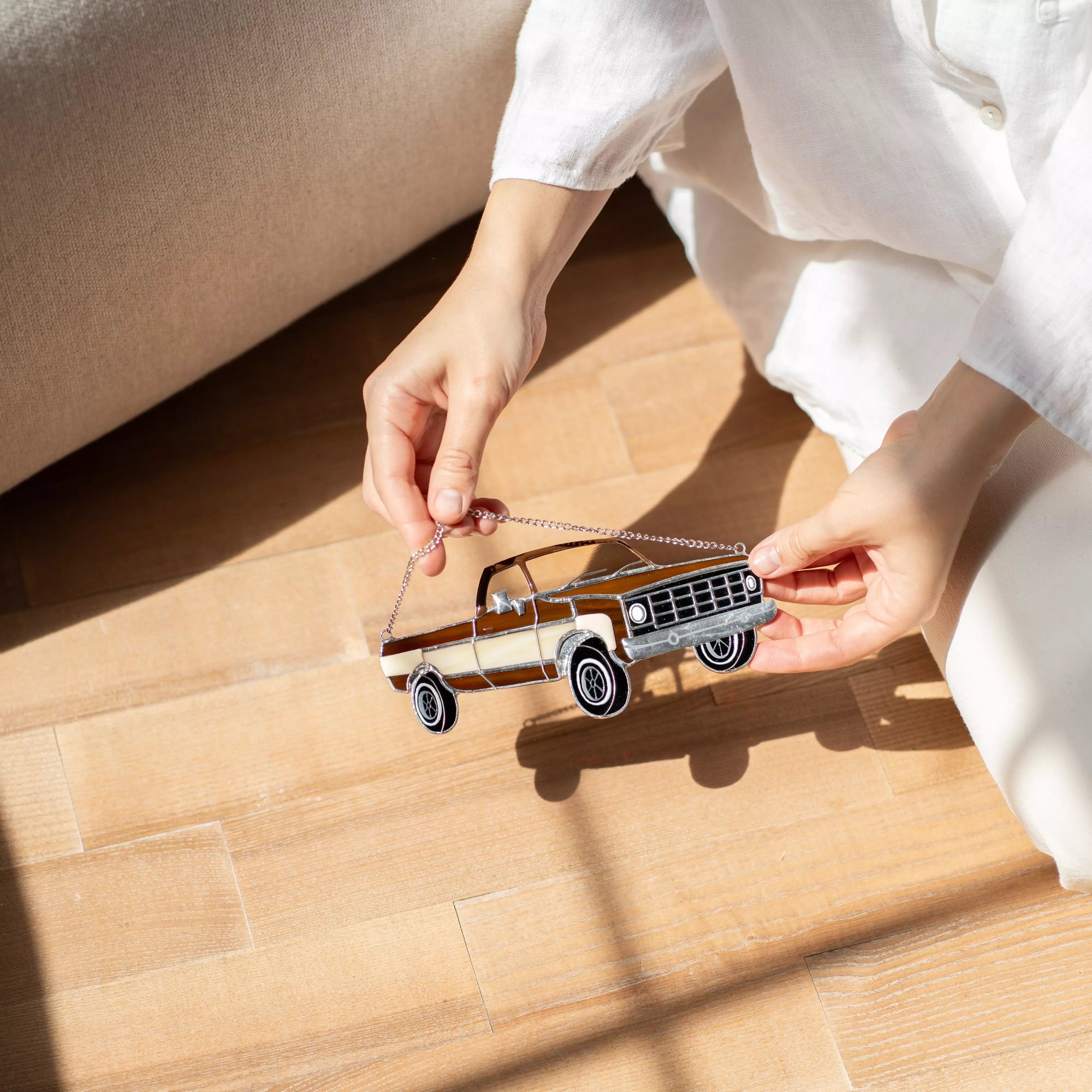 Person holding a stained glass model of a vintage truck on a wooden floor.