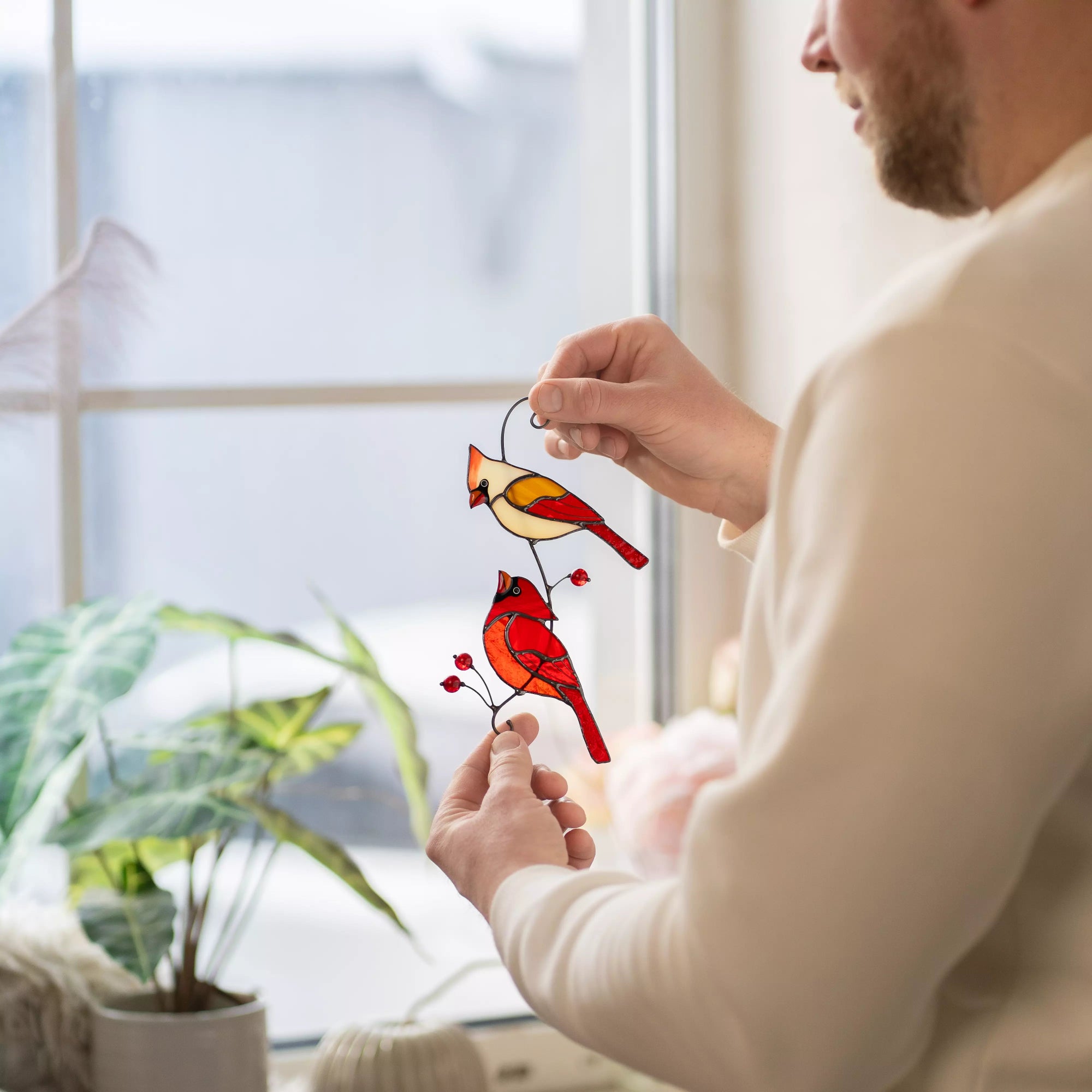 Man holding a stained glass pair of cardinals decoration in front of a window