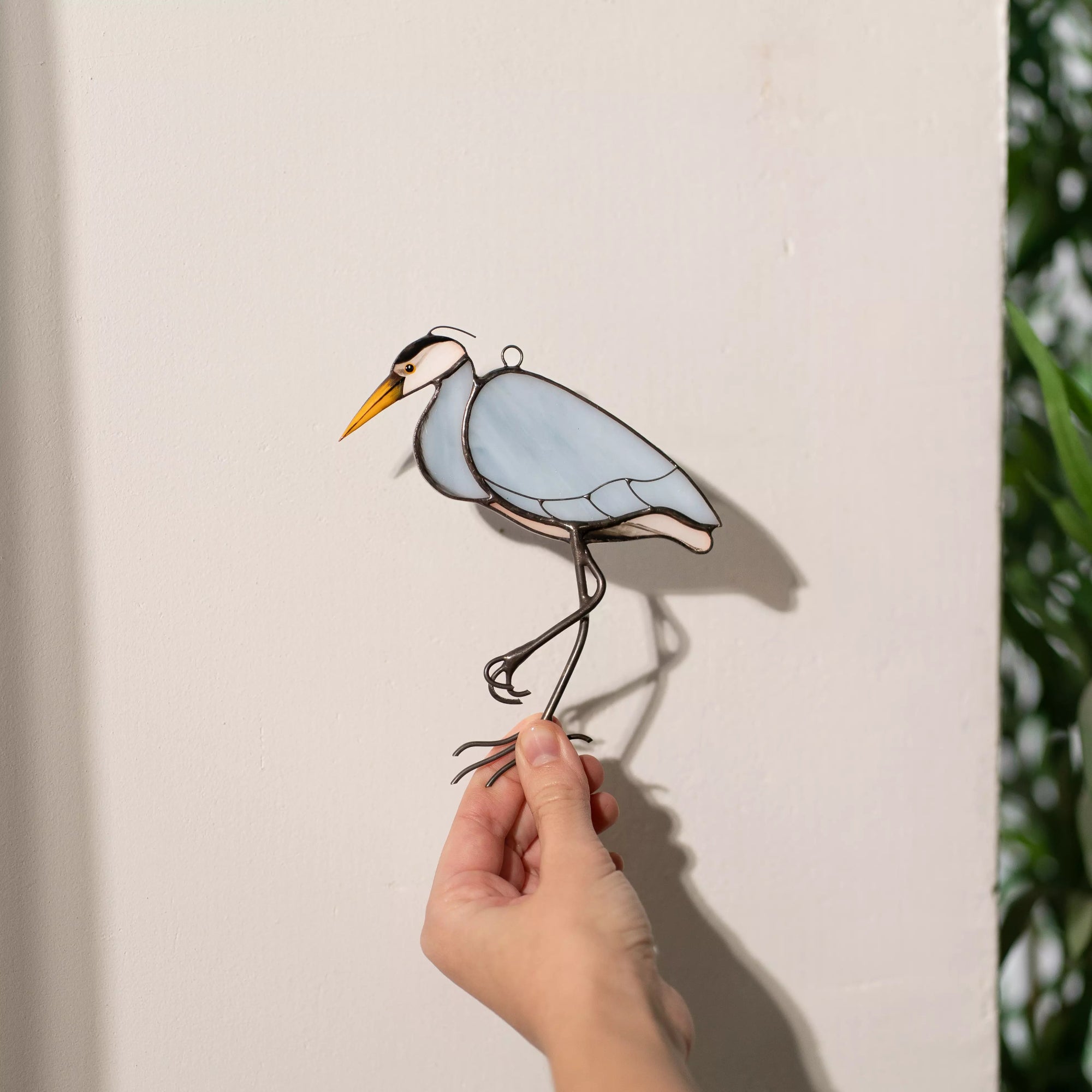 Hand holding a stained glass heron suncatcher against a light background