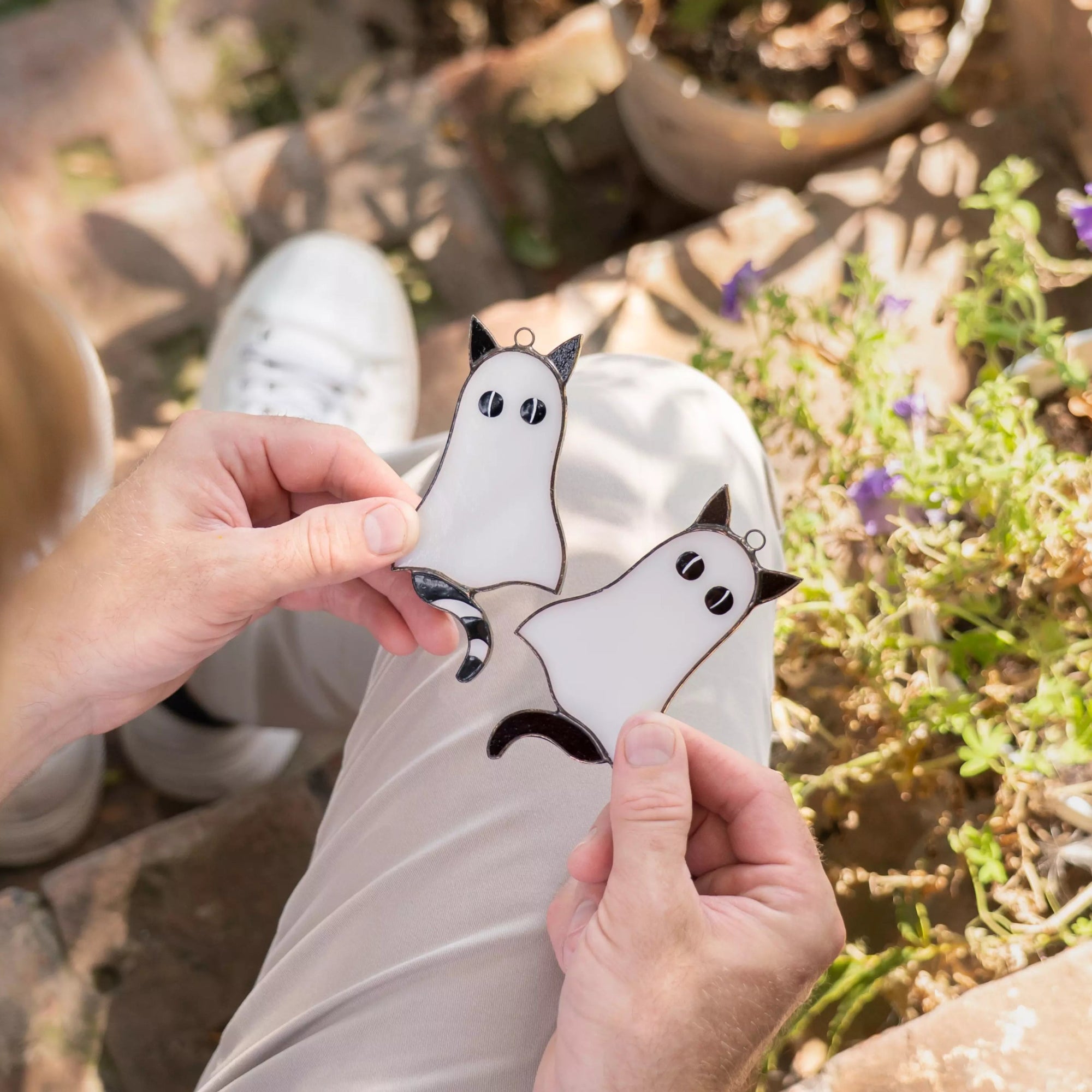 Person holding a white stained glass suncatchers with cat-ghosts design outdoors