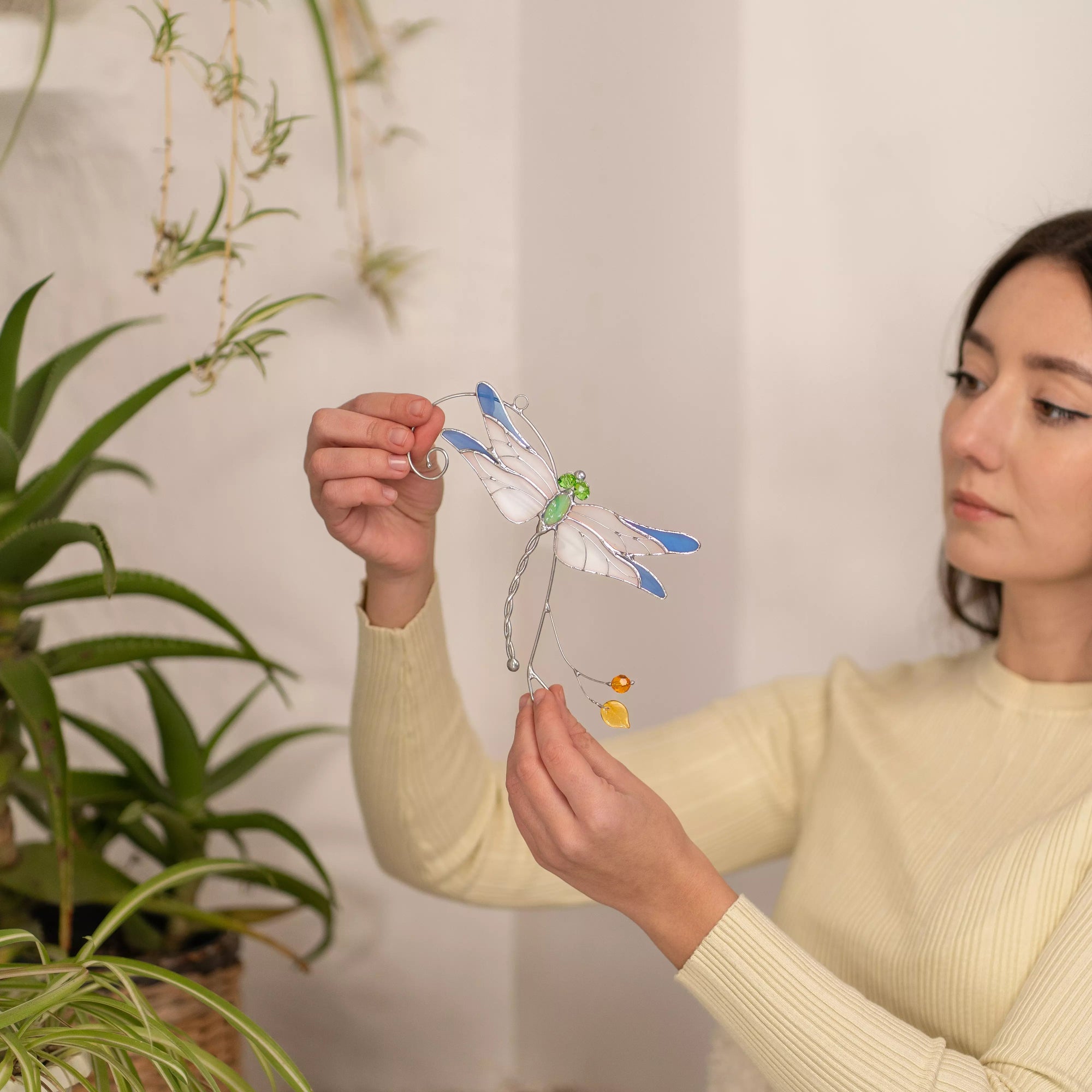 Woman holding stained glass dragonfly suncatcher in front of a plant