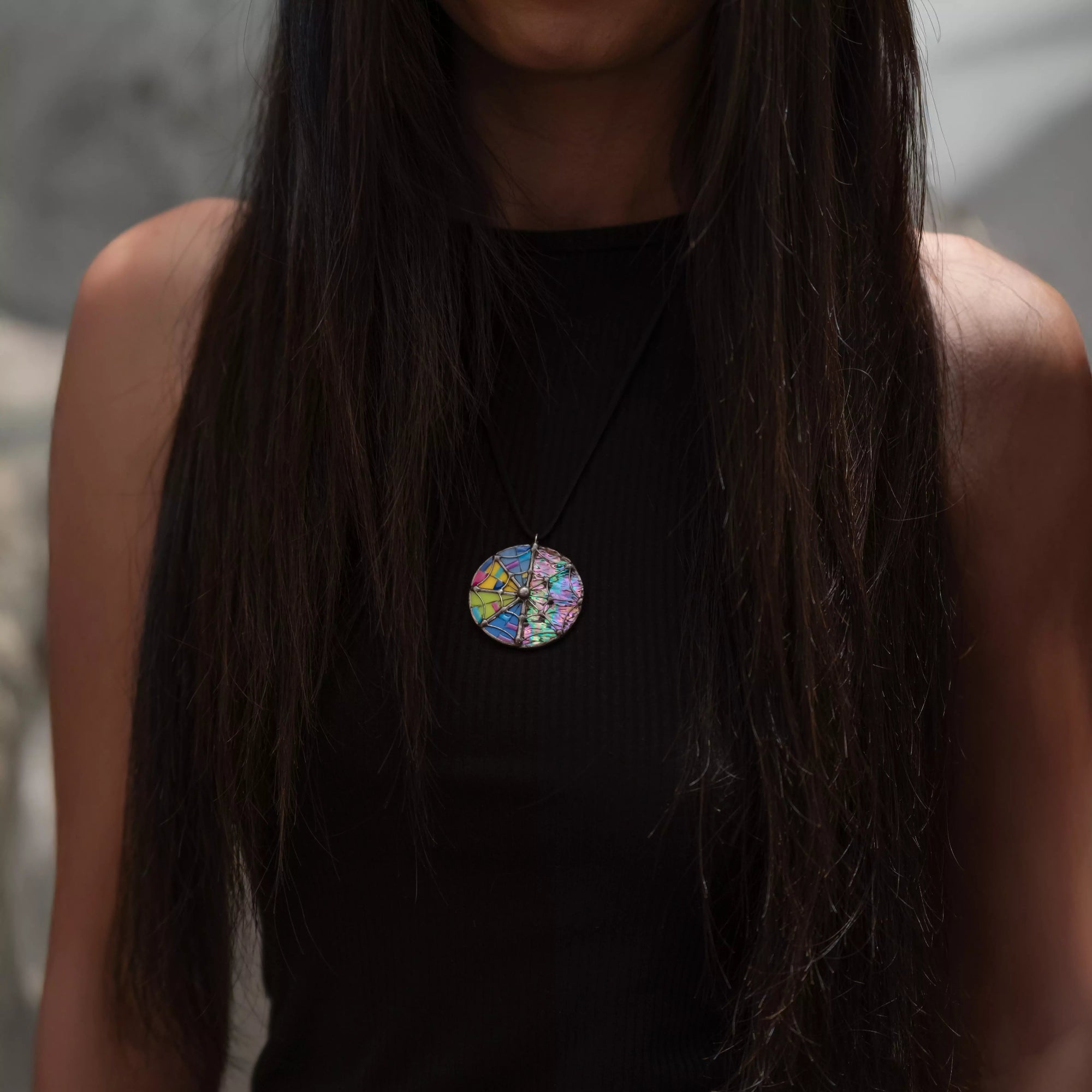 Person wearing a colorful stained glass irizated pendant with web necklace against a neutral background