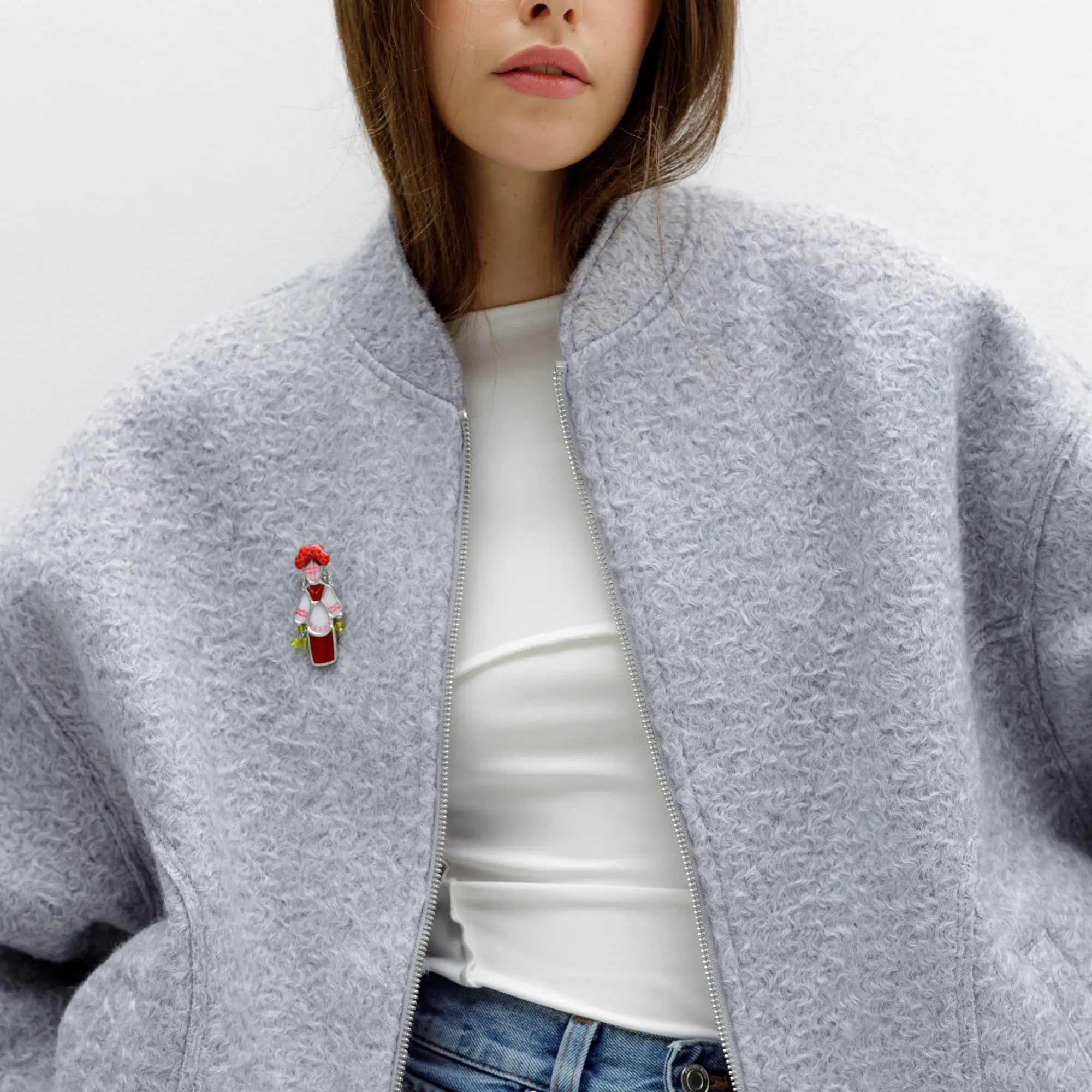 Person wearing a gray jacket with a stained glass brooch colored red and white on a plain background