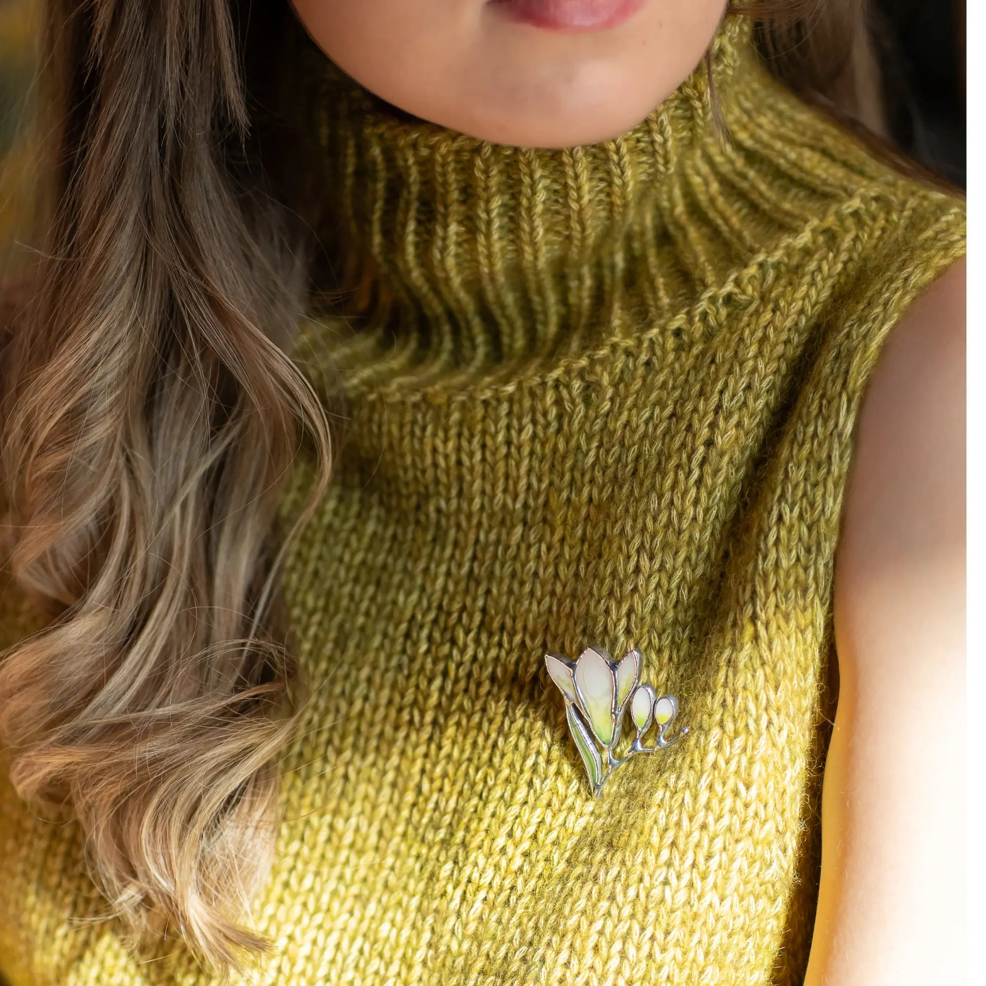 Women wearing a green sleeveless sweater with a stained glass white freesia brooch.