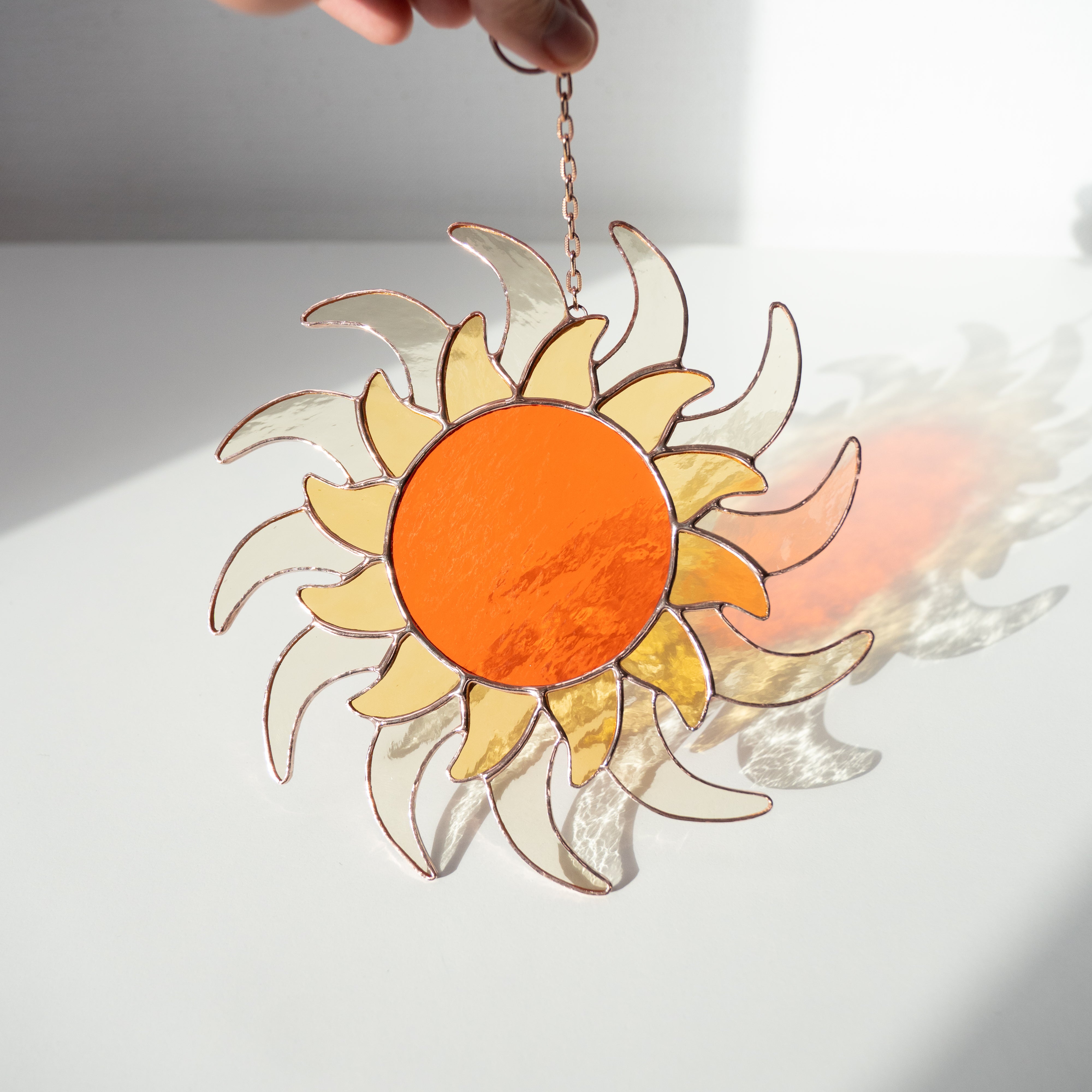 Stained glass sun suncatcher casting detailed reflections on a white surface in bright direct light.
