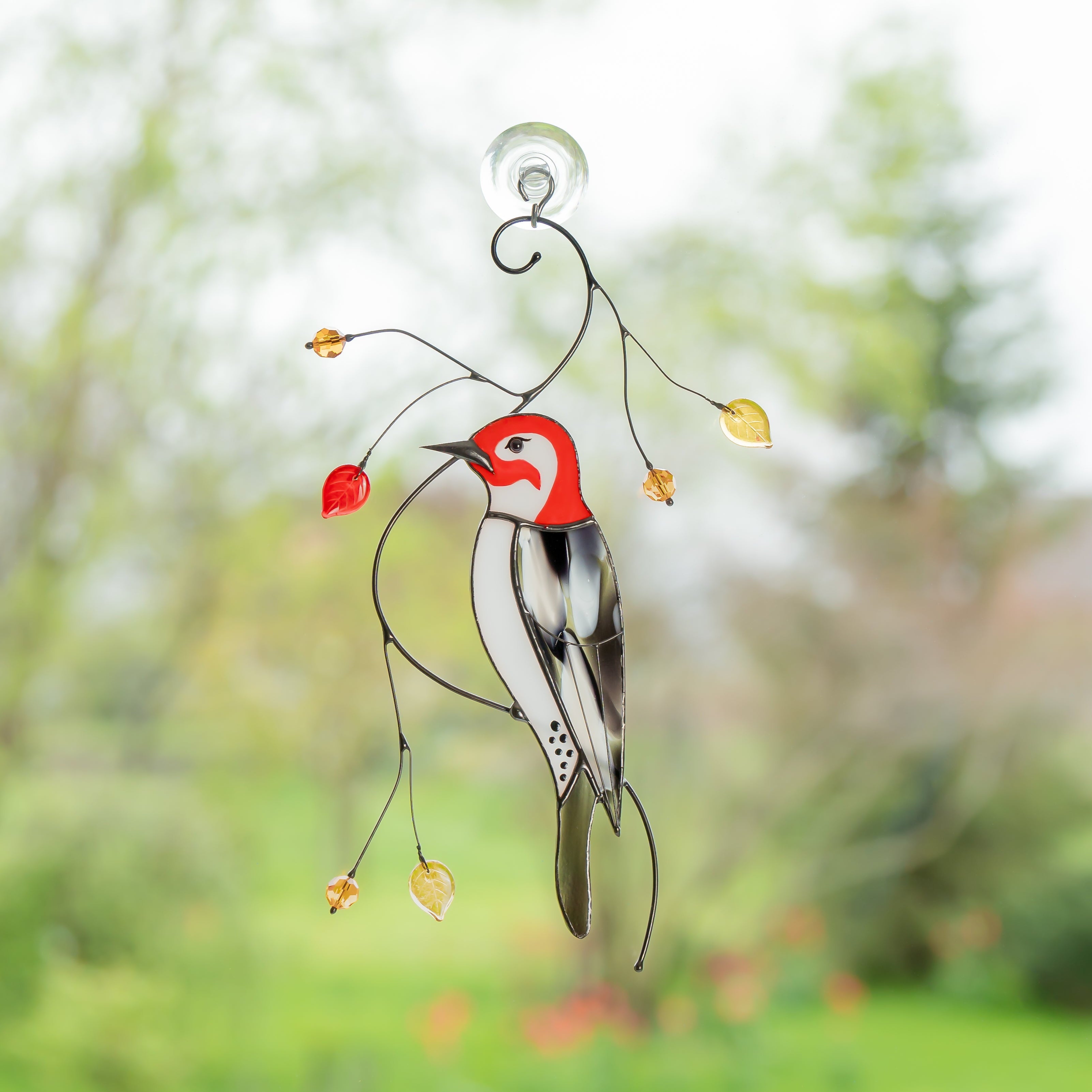 Stained glass woodpecker suncatcher with red head and glass golden leaves, hanging on a window with a suction cup.