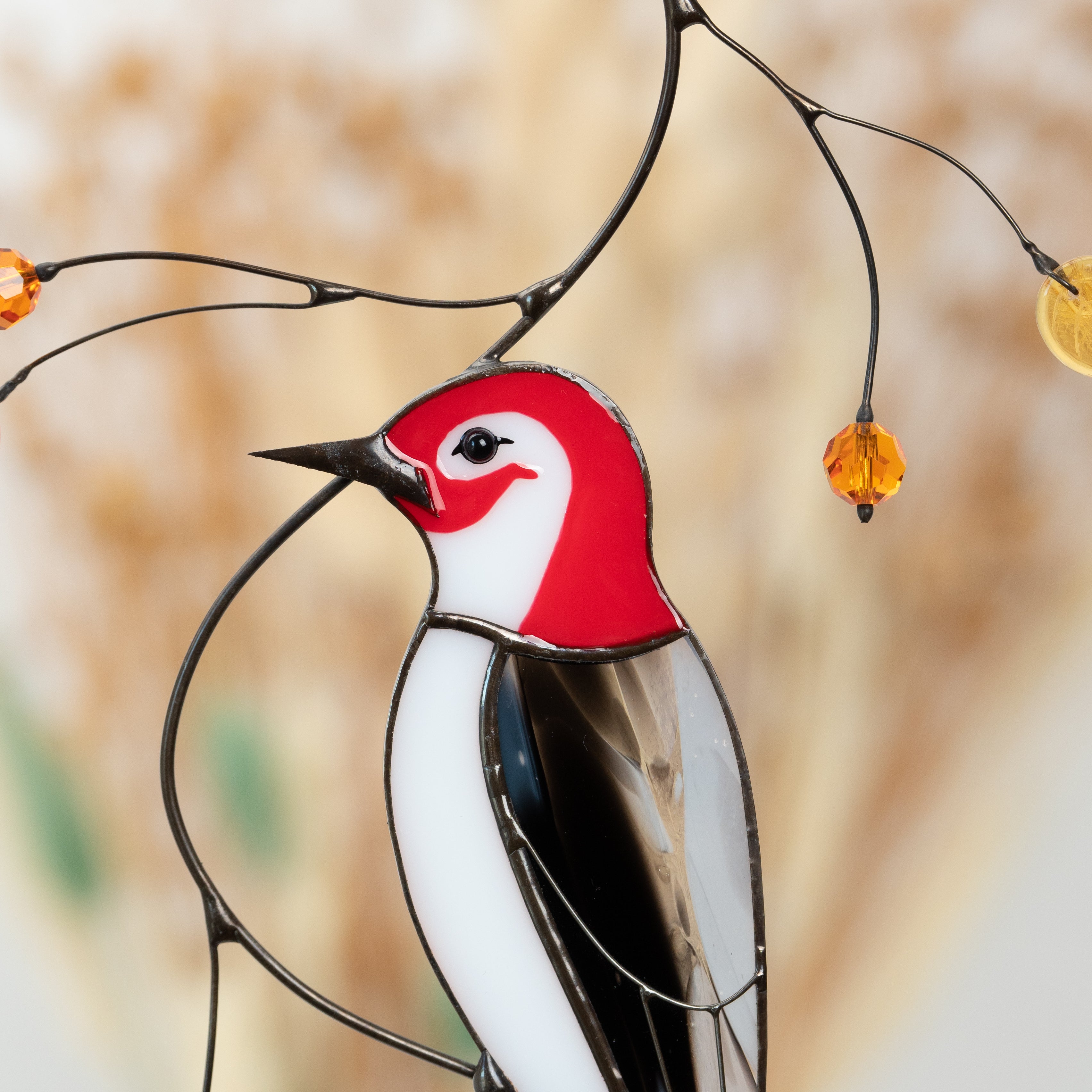 Close-up of a stained glass woodpecker head with red and white details, hanging on curved wire with golden leaves