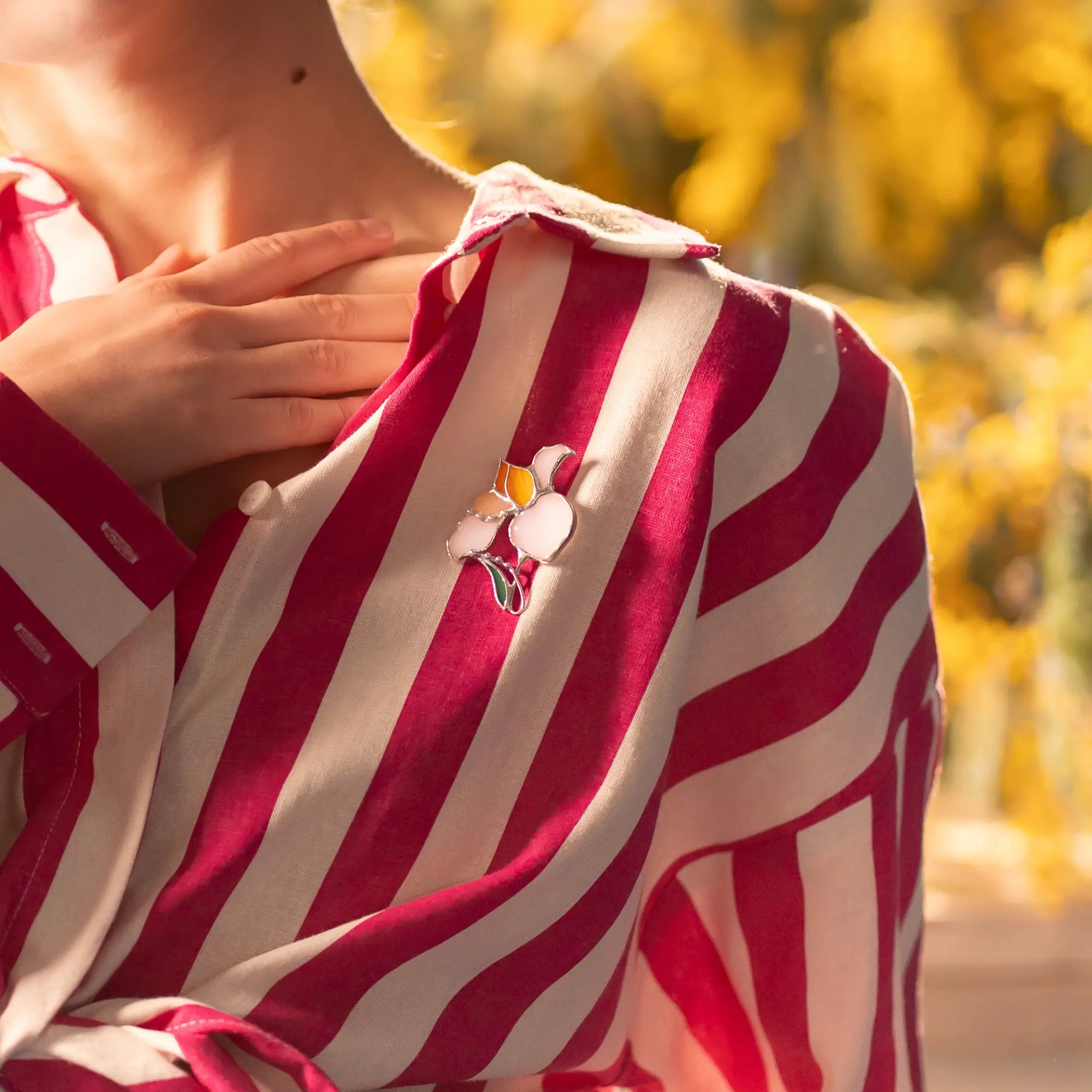 Pink and white striped shirt with a floral stained glass brooch worn by a person, blurred yellow background