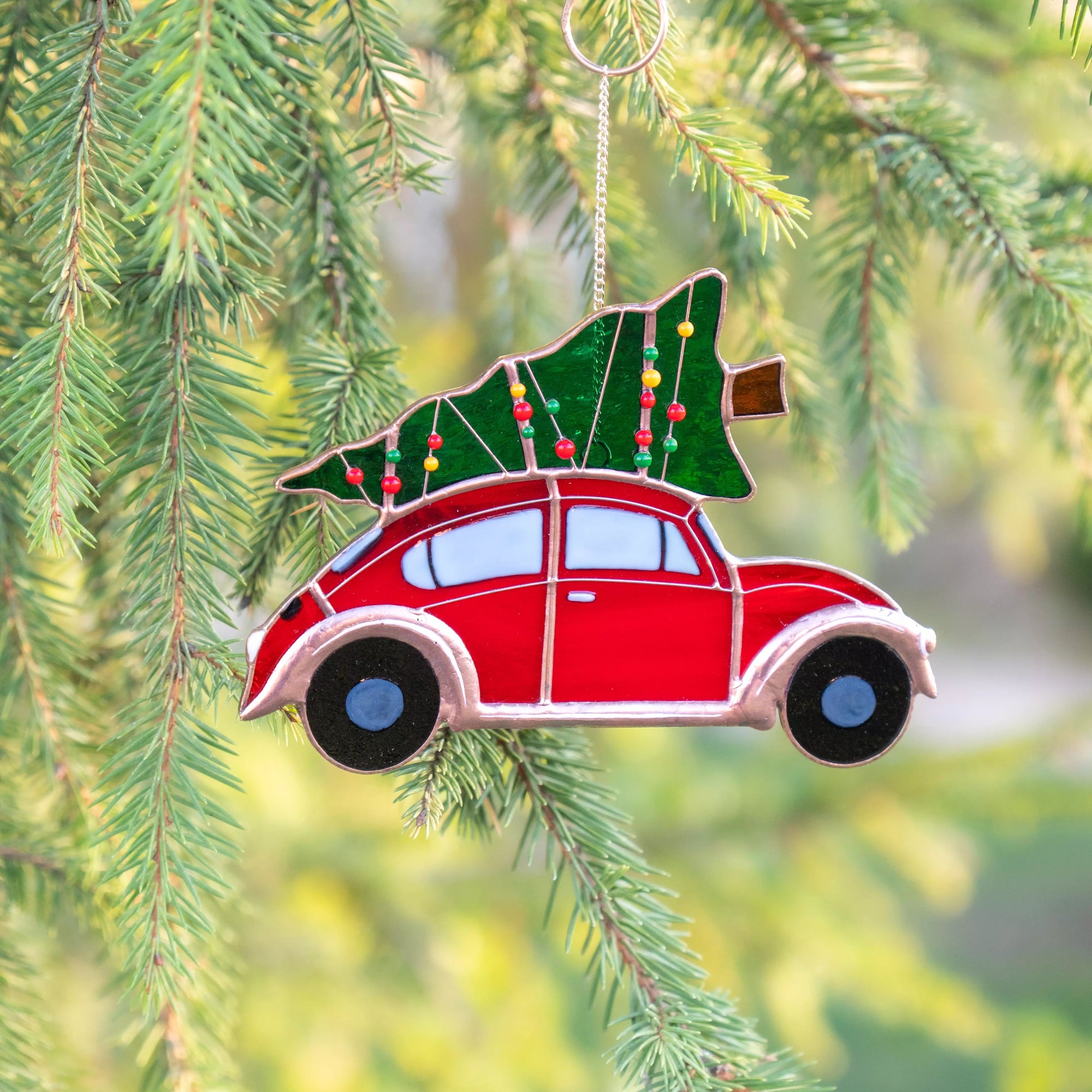 Red car ornament with a green tree on top stained glass suncatcher, hanging from a branch.