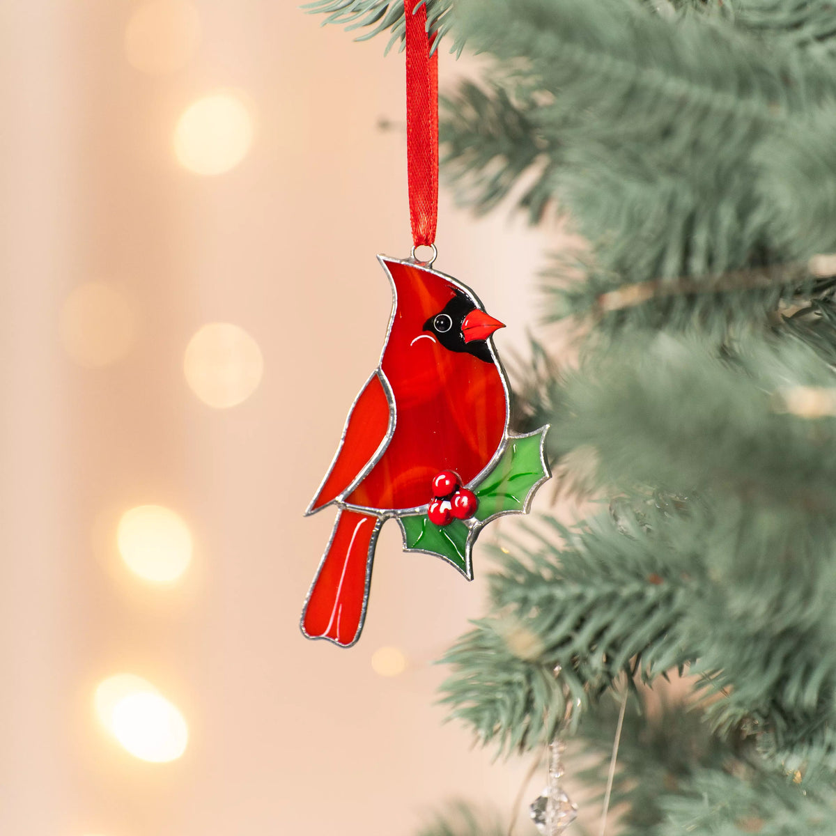 Stained glass red cardinal ornament with holly leaves on a Christmas tree