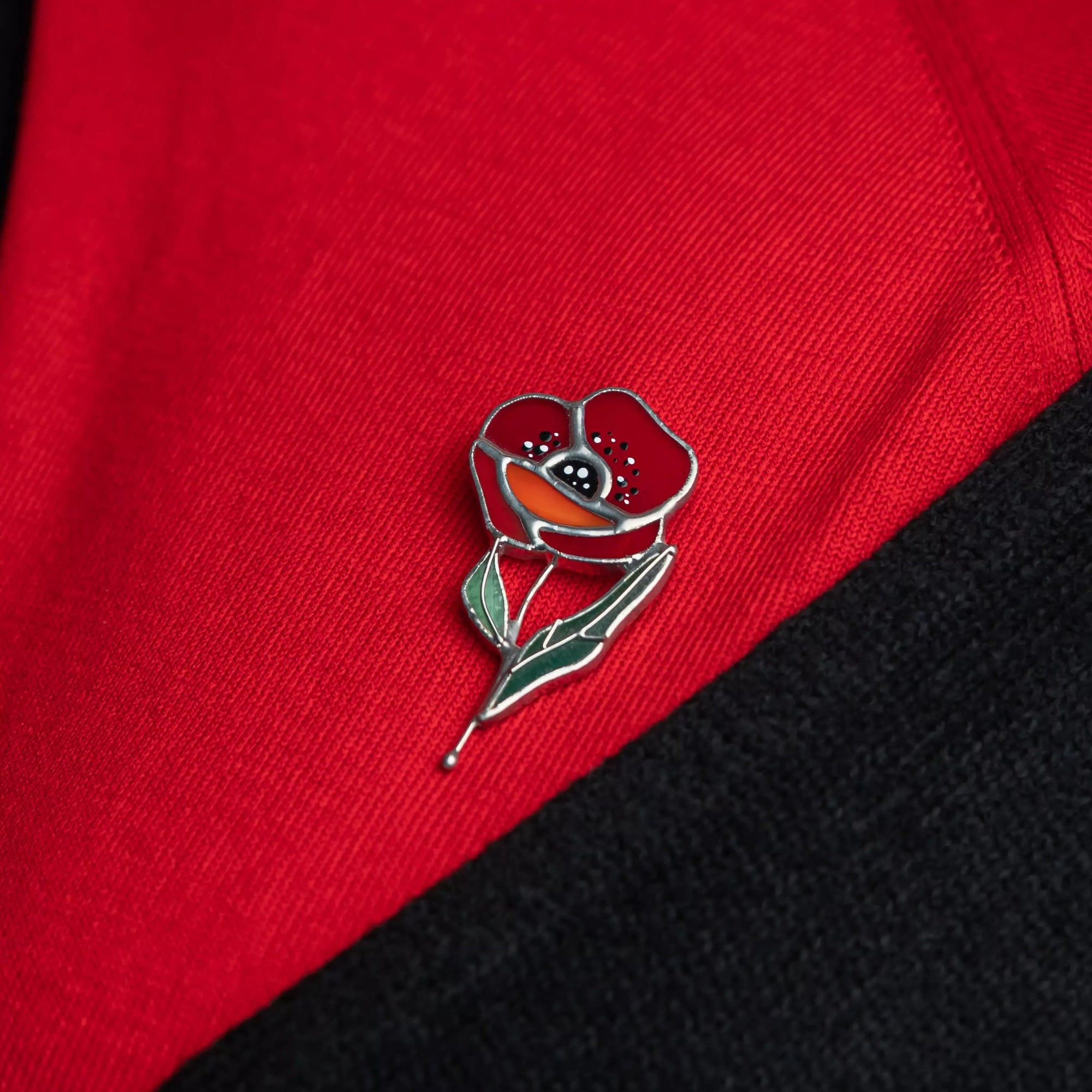 Red poppy stained glass pin on a red and black fabric background