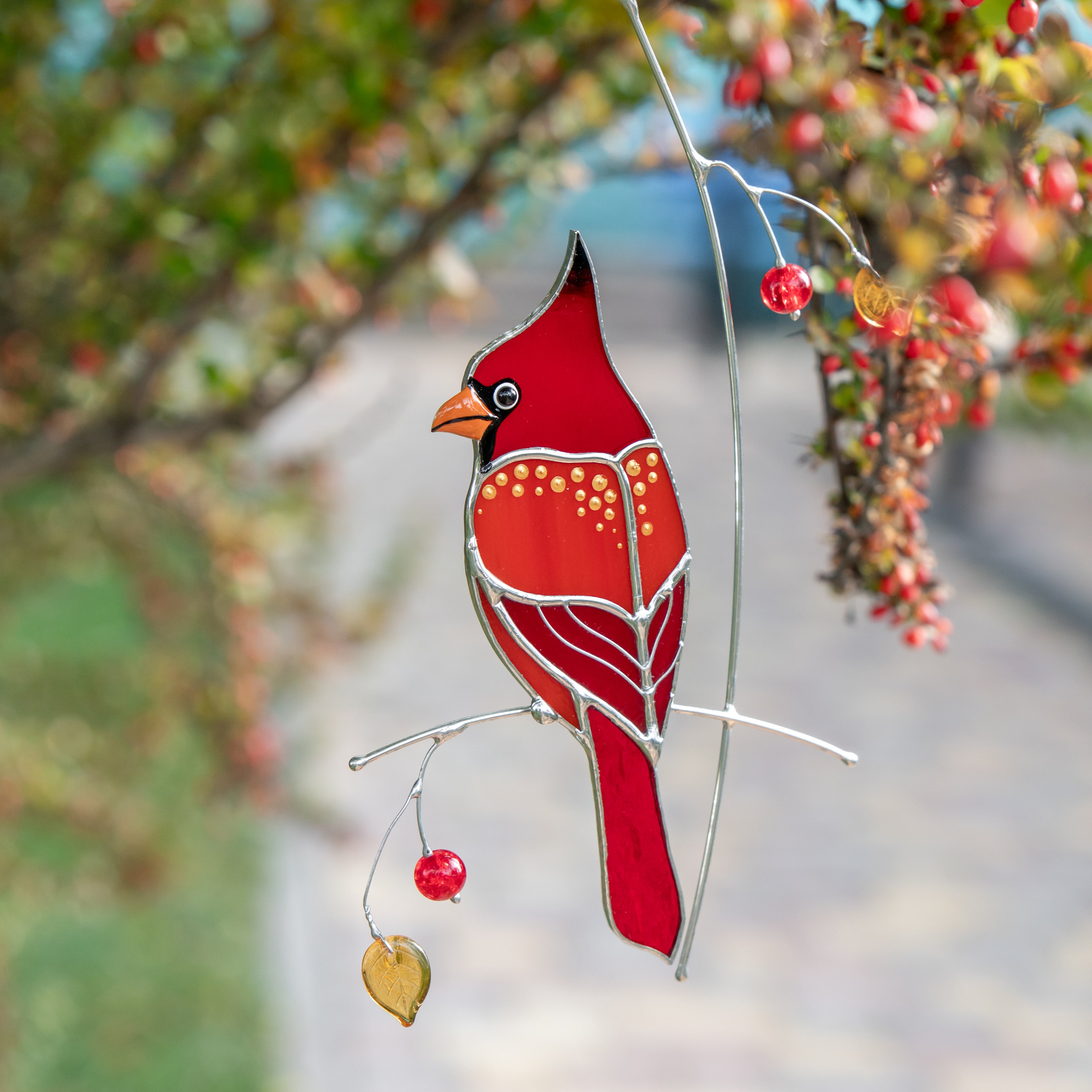 Stained glass cardinal with beads and golden details hanging among autumn branches.