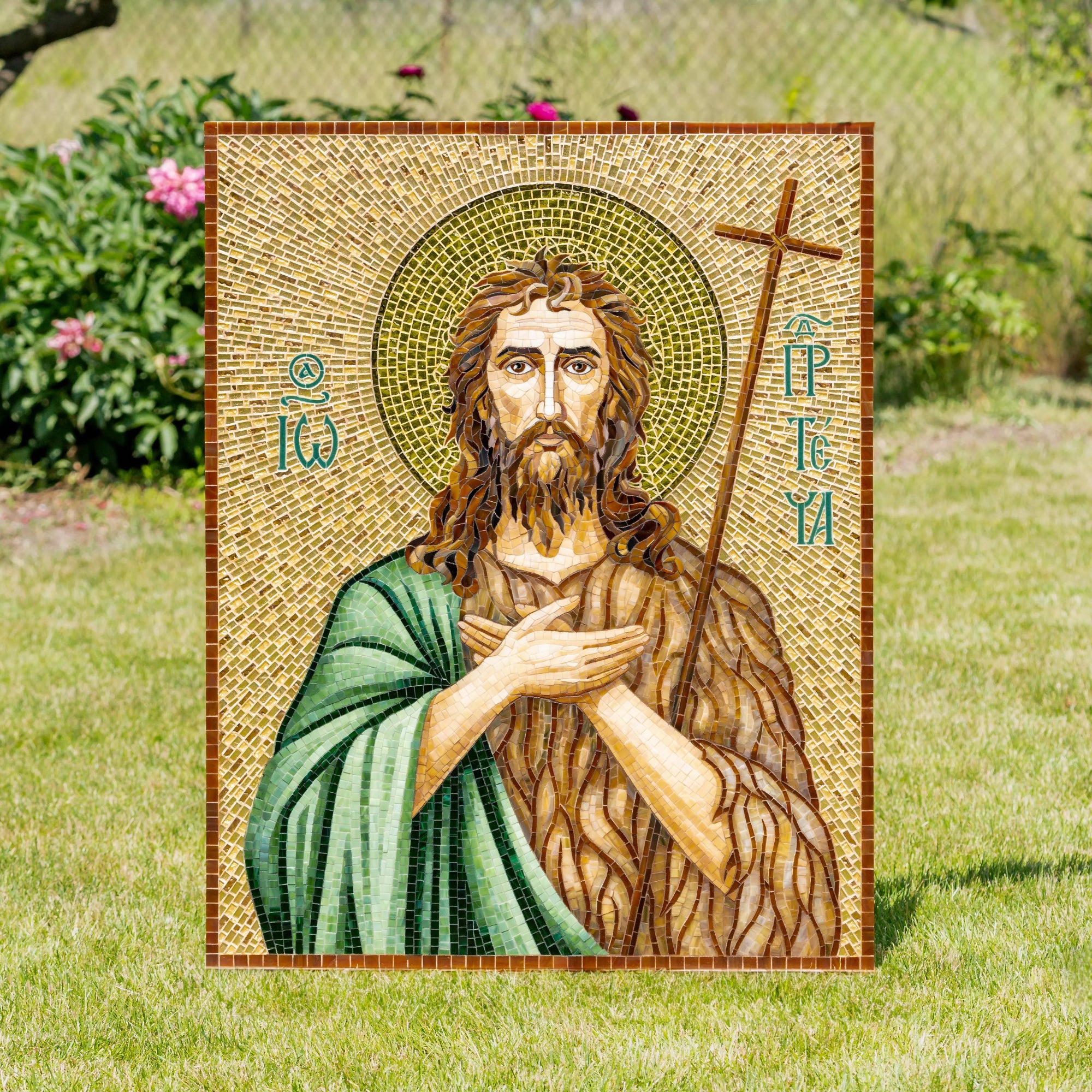 Icon of Saint John the Baptist mosaic outdoors with visible greenery and flowers