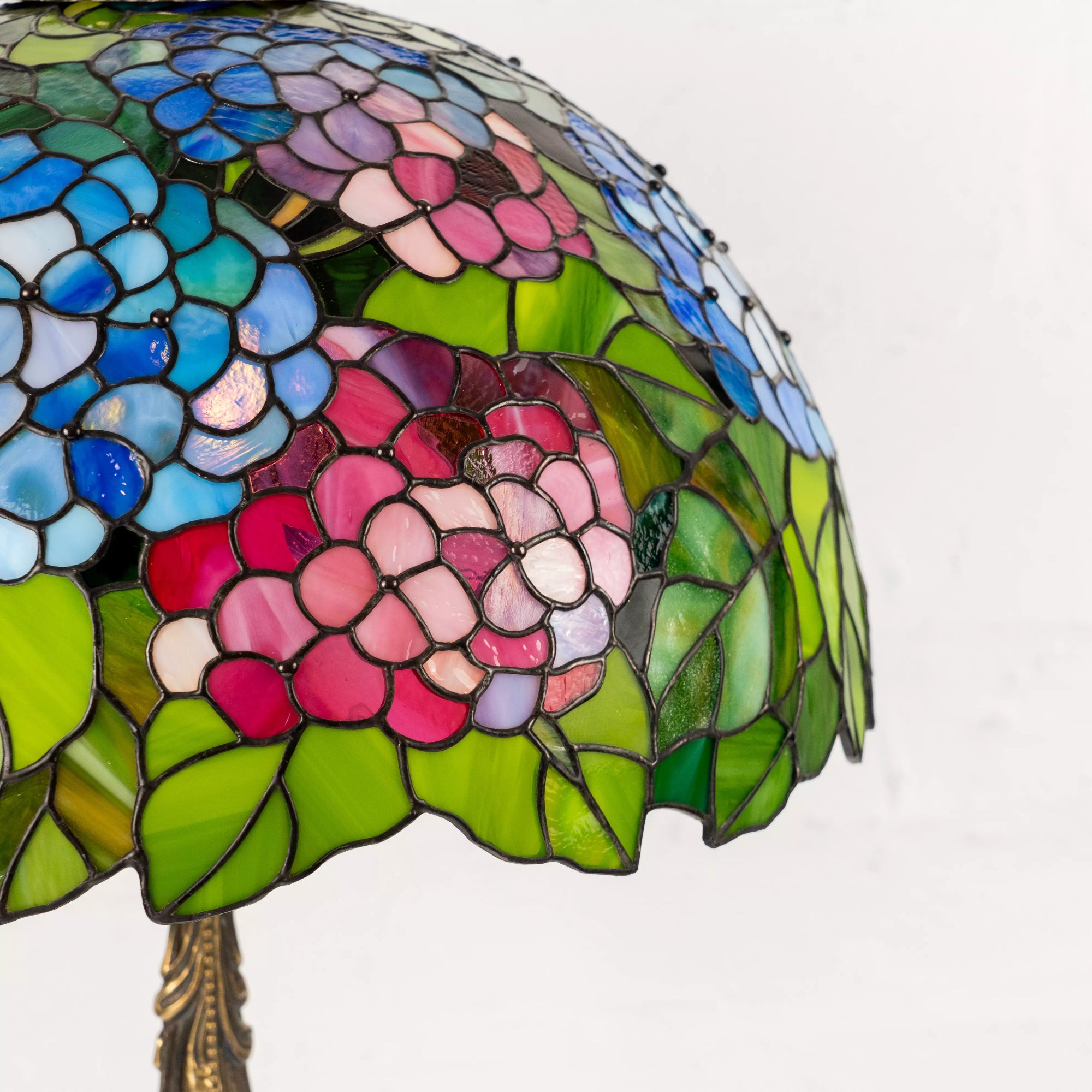 Close view of curved stained glass hydrangeas and foliage on vintage lamp shade.