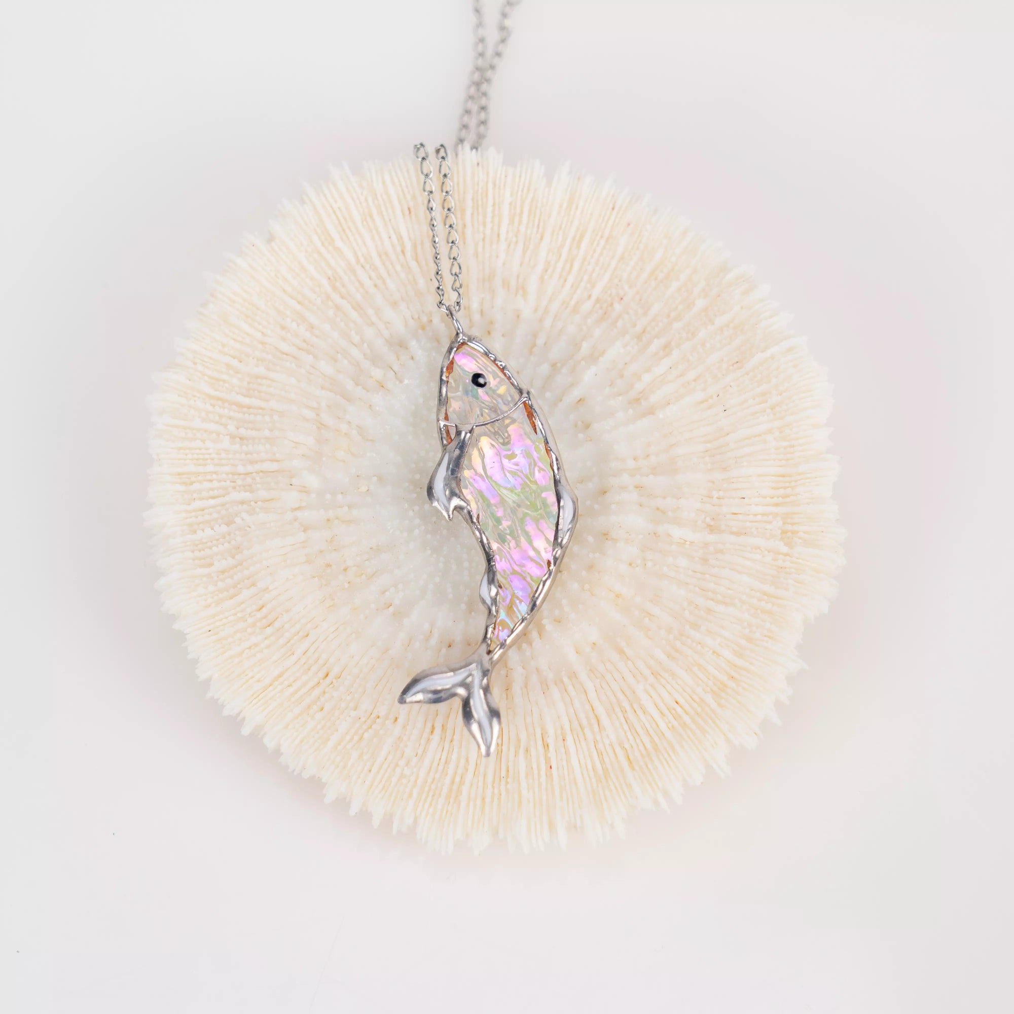 Light-catching stained glass fish pendant resting on a pale, round textured coral
