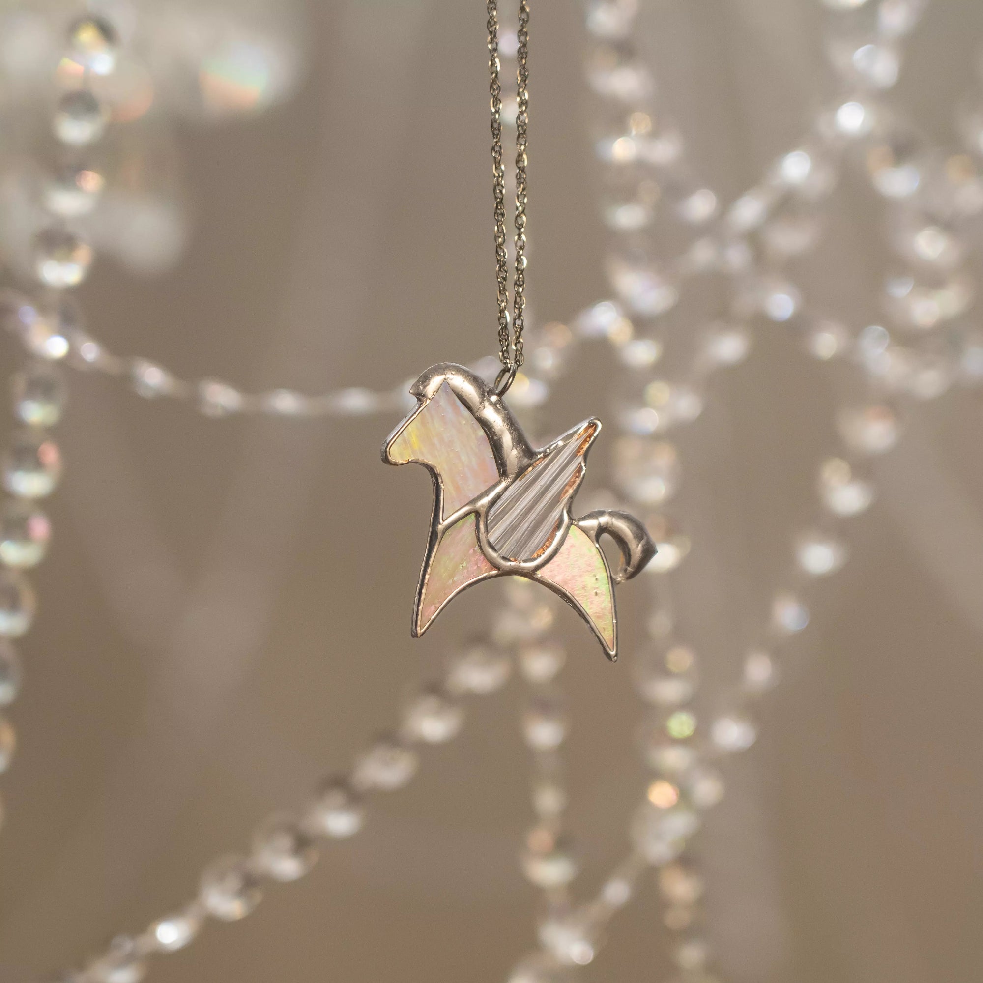 Silver necklace with a stained glass pendant shaped like a pegasus on a blurred background