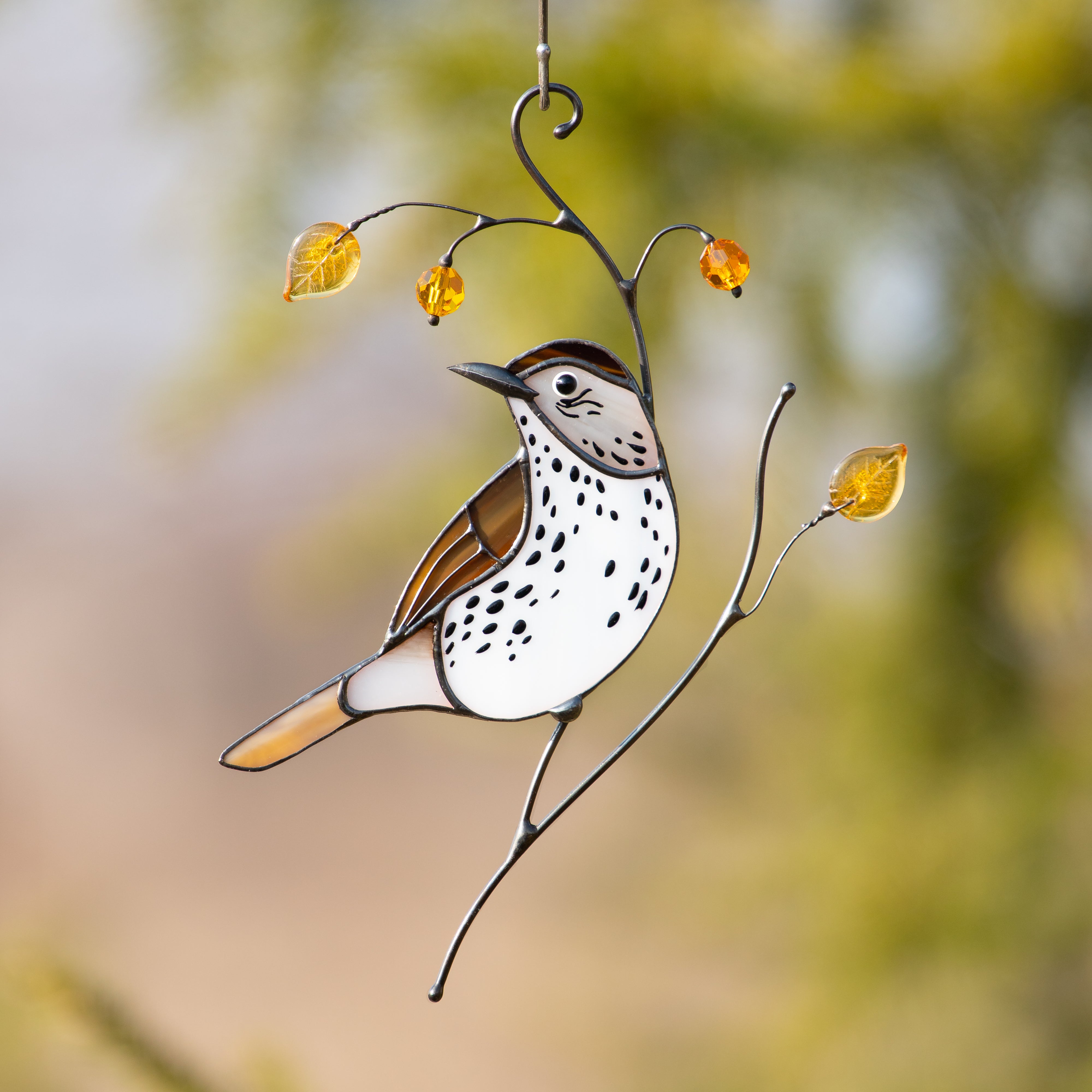 Stained glass wood thrush with speckled chest, amber beads, and golden glass leaves in sunlight