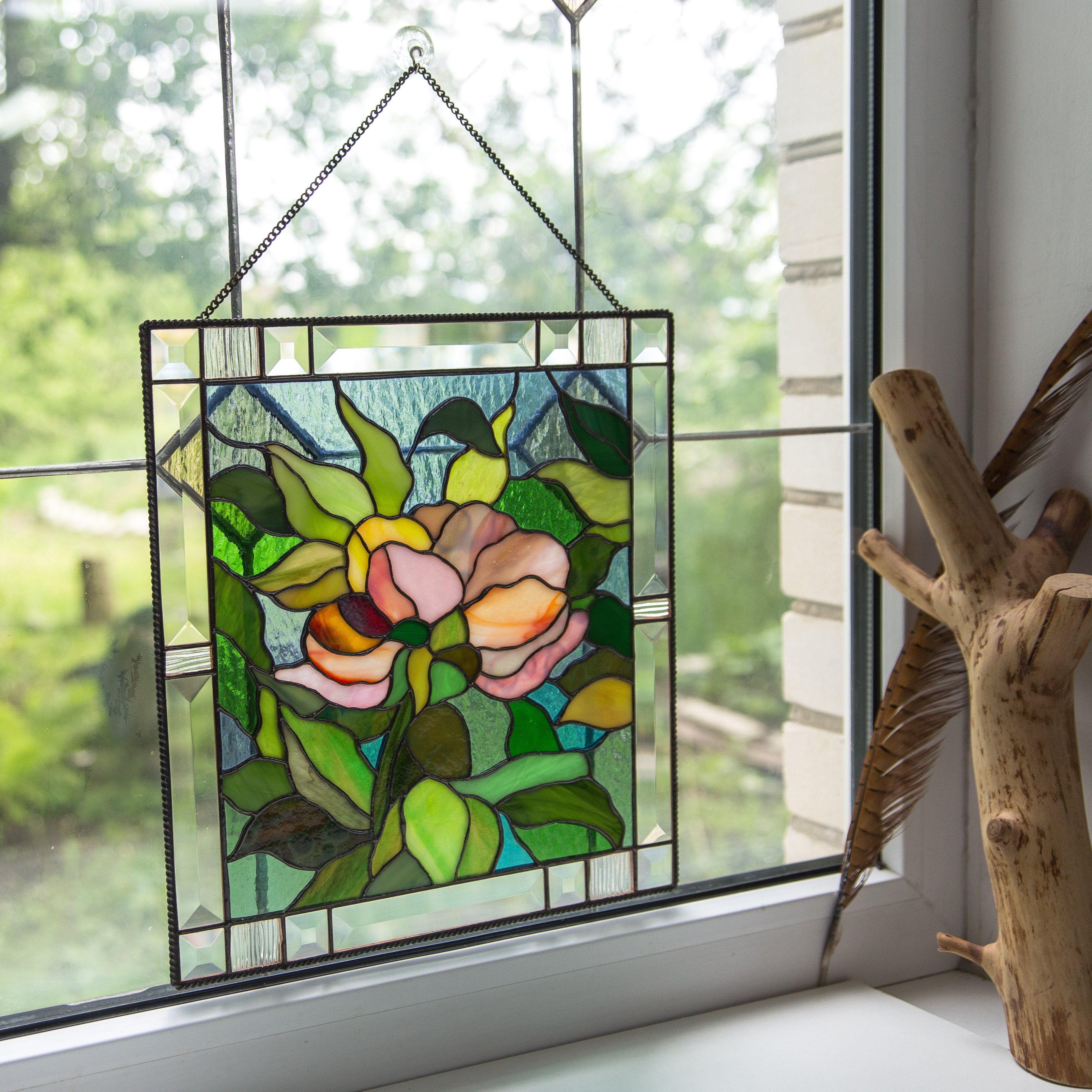 Stained glass panel with peony bud design hanging on a window