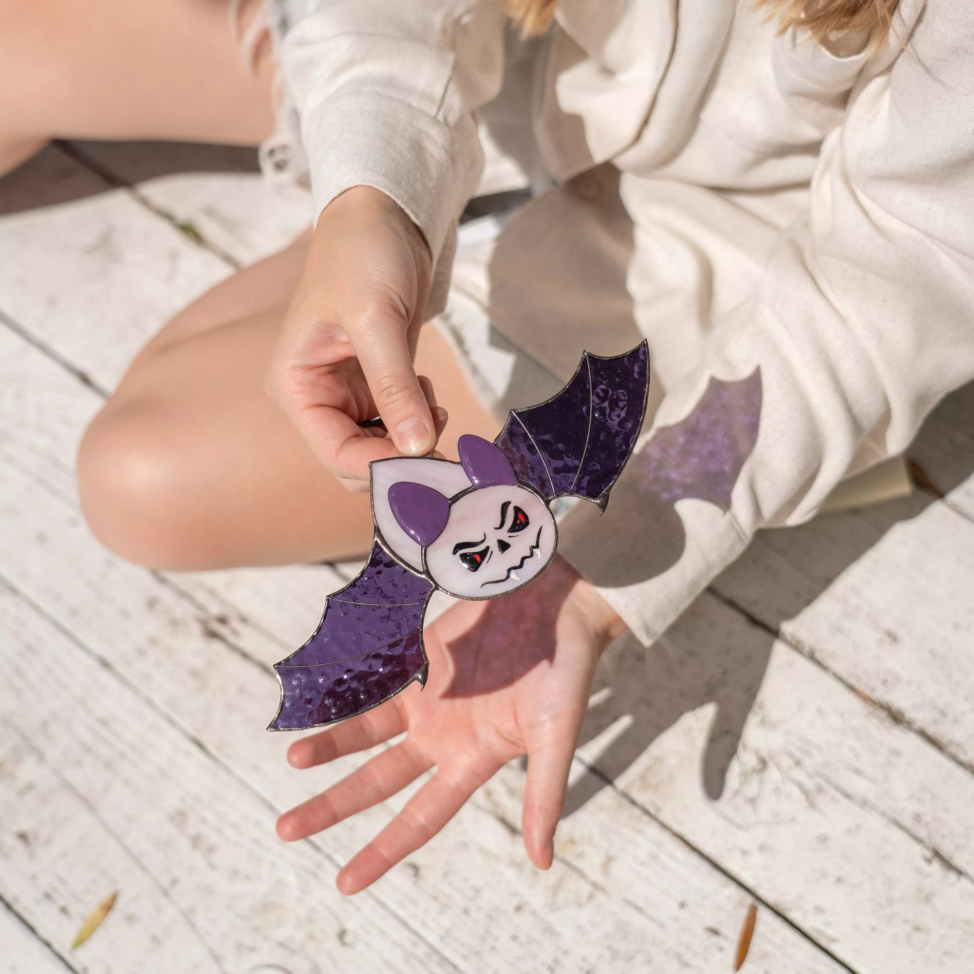 Person holding purple stained glass bat with scary face in sunlight