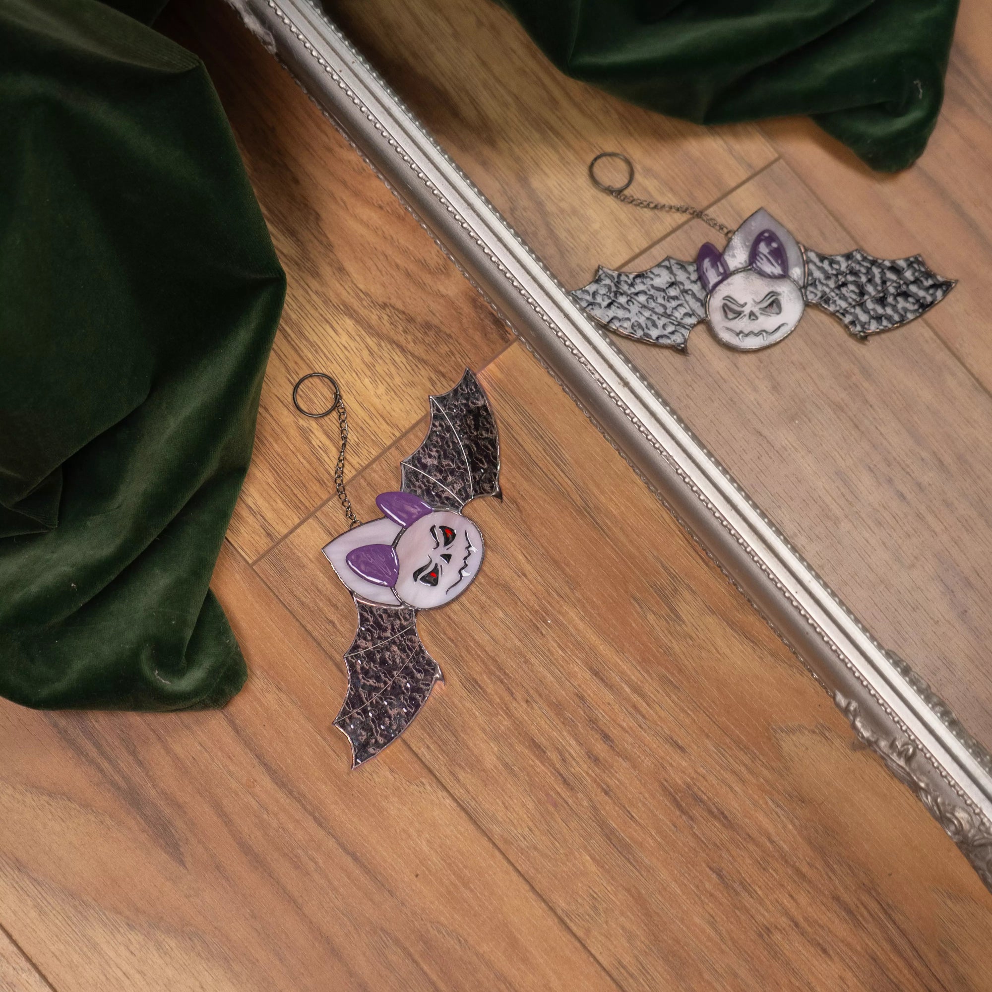 Purple stained glass bat with spooky face lying by mirror with reflection