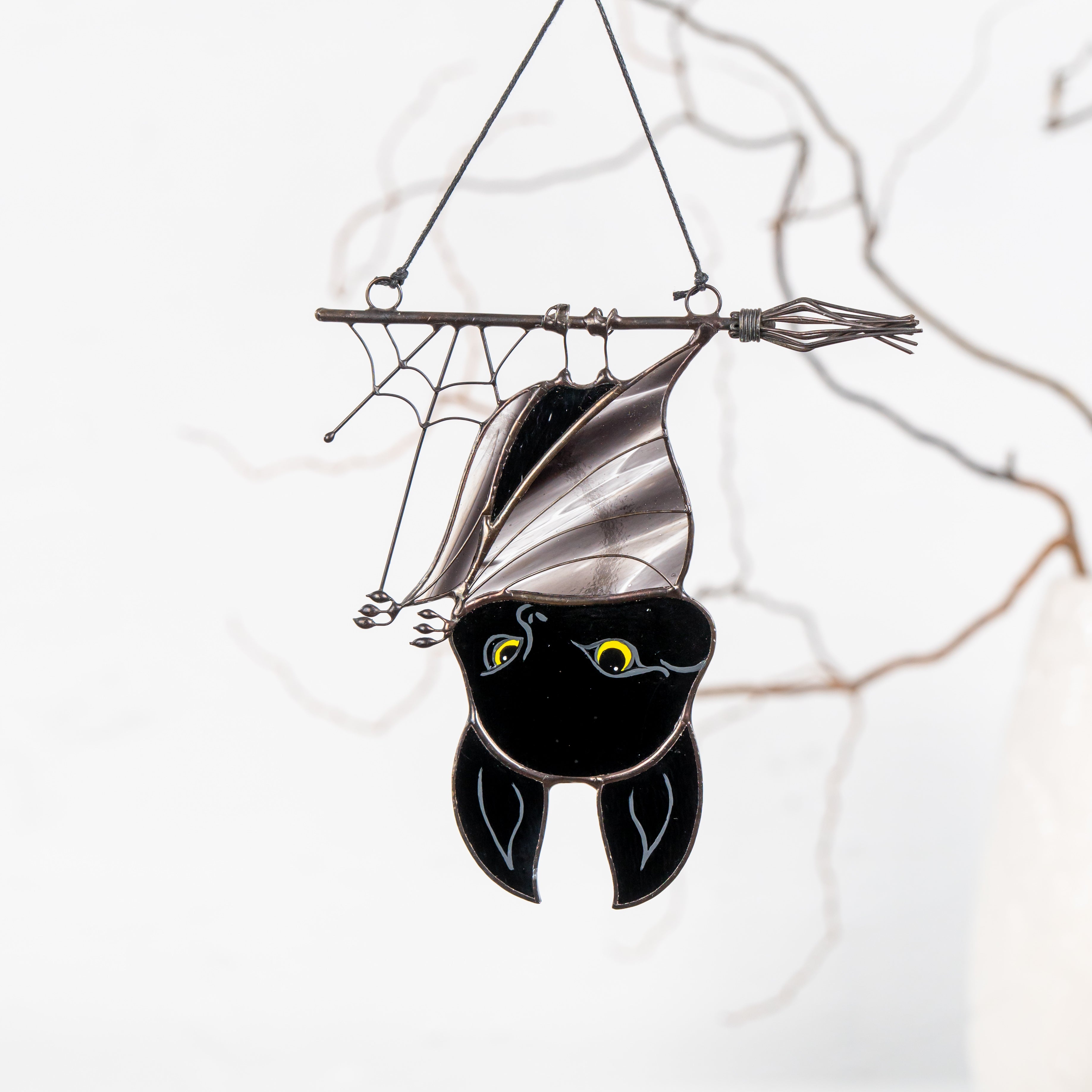 Stained glass bat hanging from a witch’s broom with cobweb detail, ideal for Halloween window decor.