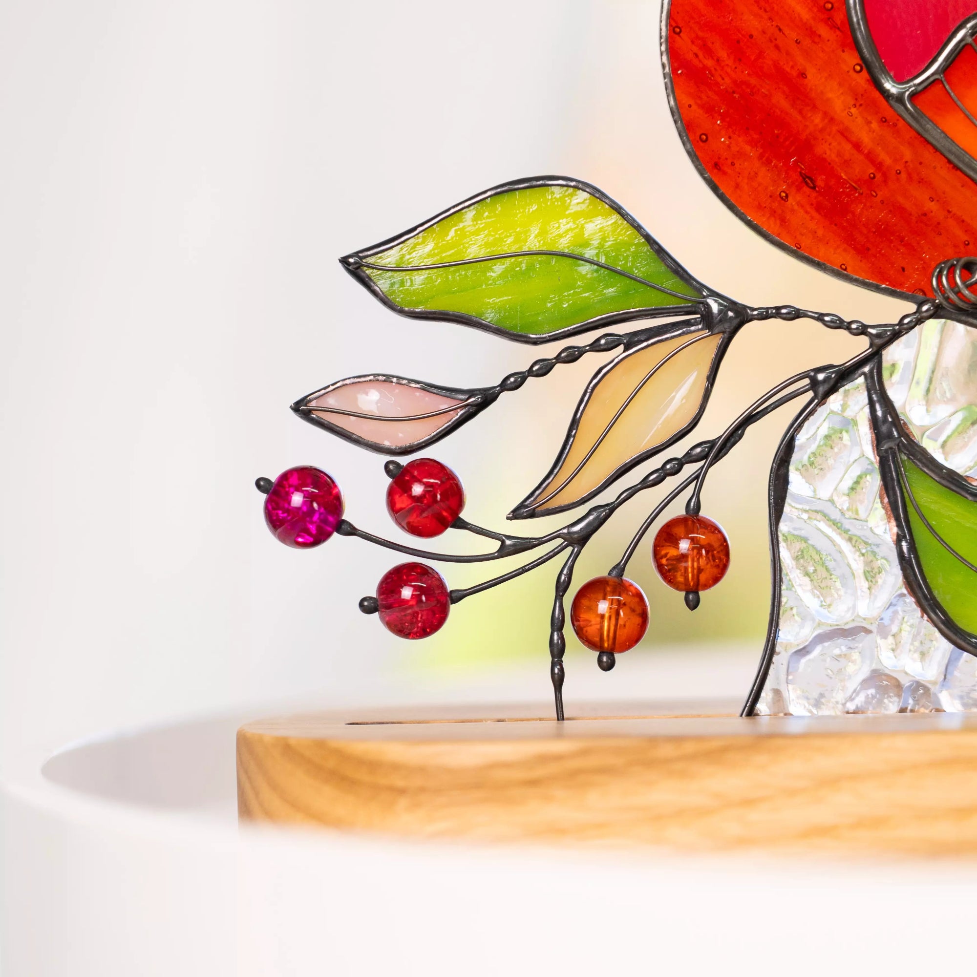 Close-up of stained glass bird branch details featuring translucent green stained glass leaves, twisted solder lines, and red and amber glass beads.