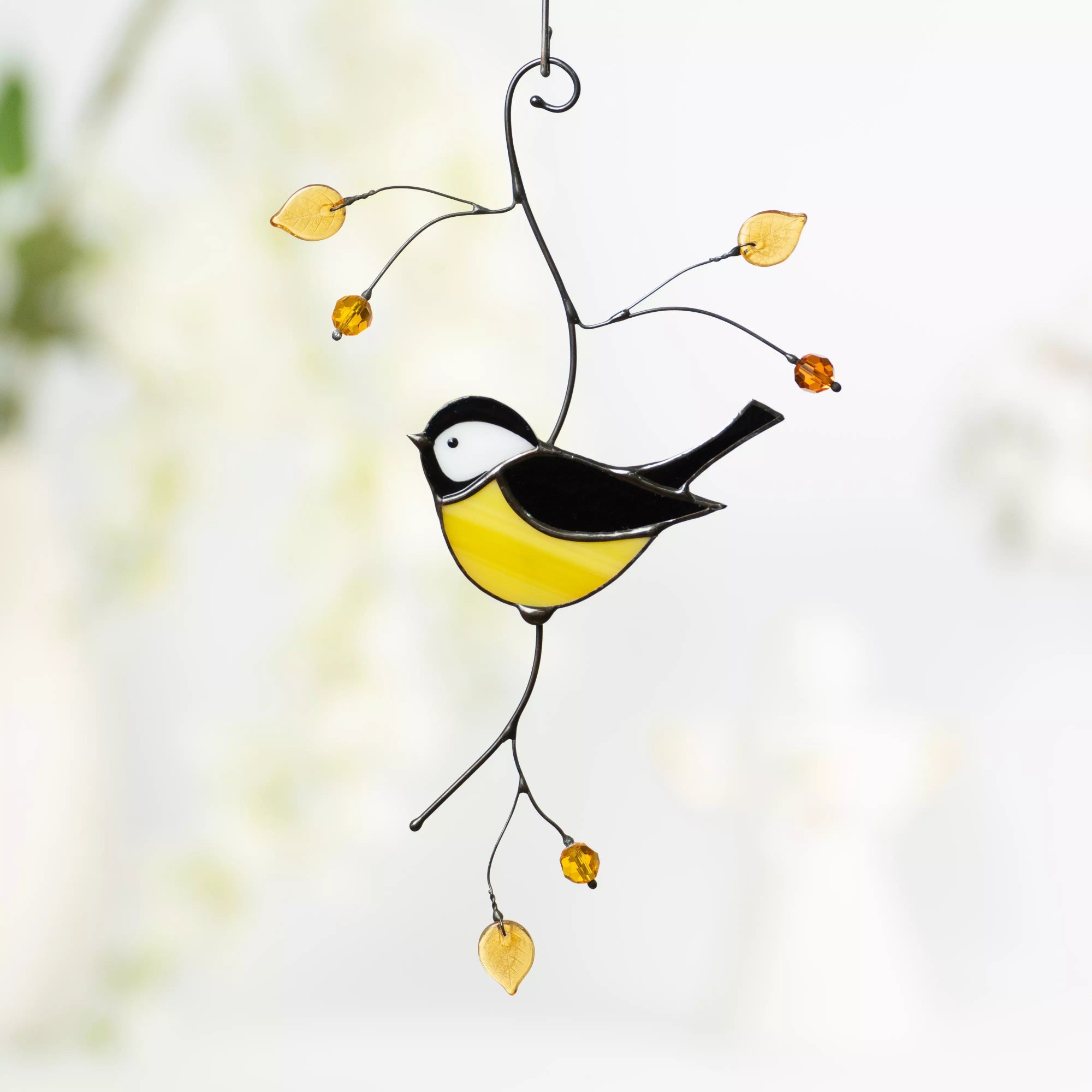 Stained glass chickadee bird hanging ornament on a blurred natural background