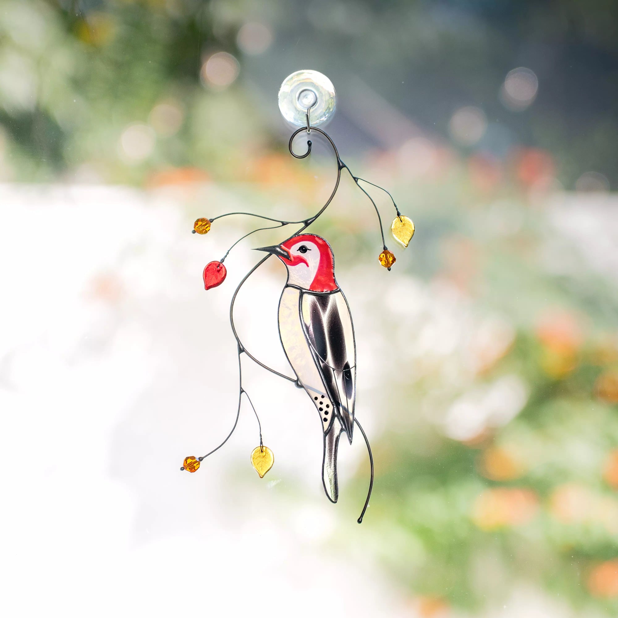 Stained glass woodpecker suncatcher with leaves against a blurred natural background