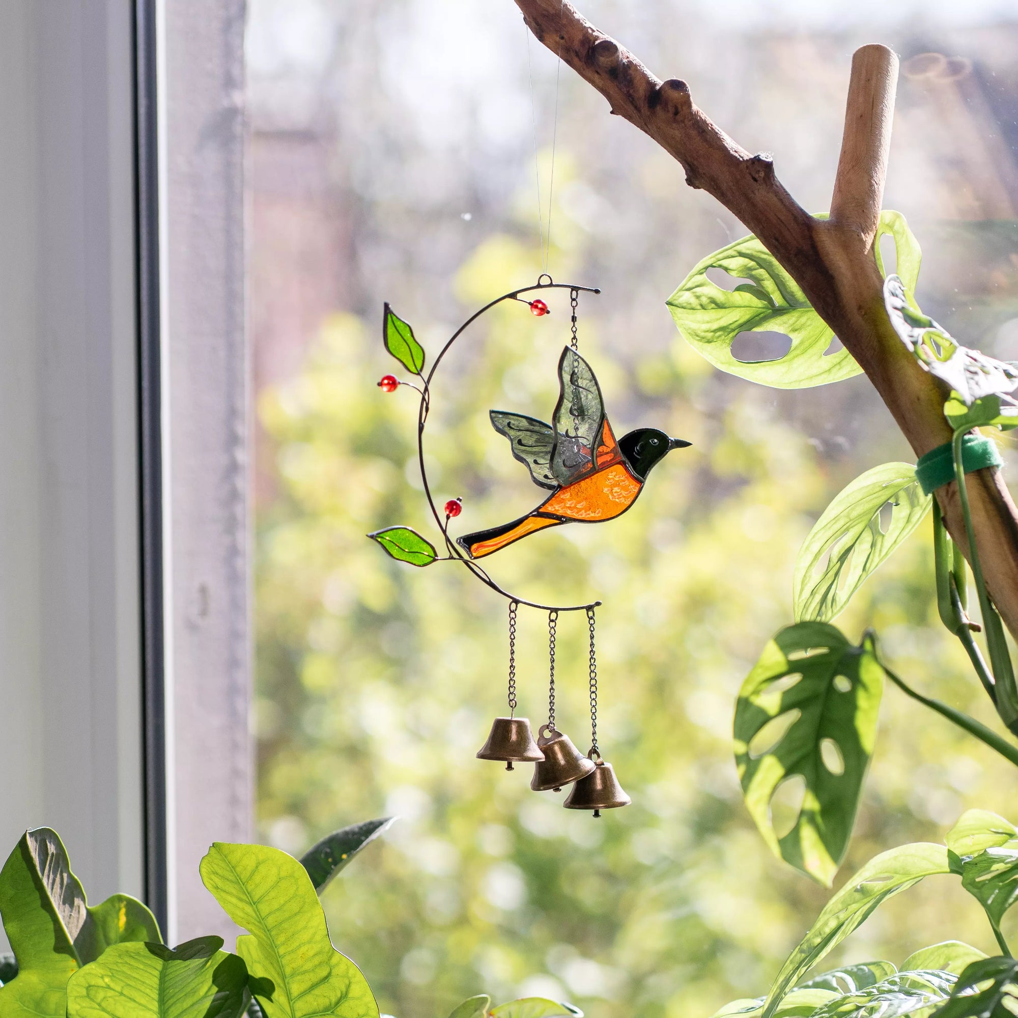 Decorative stained glass bird with bells wind chime on a branch indoors.